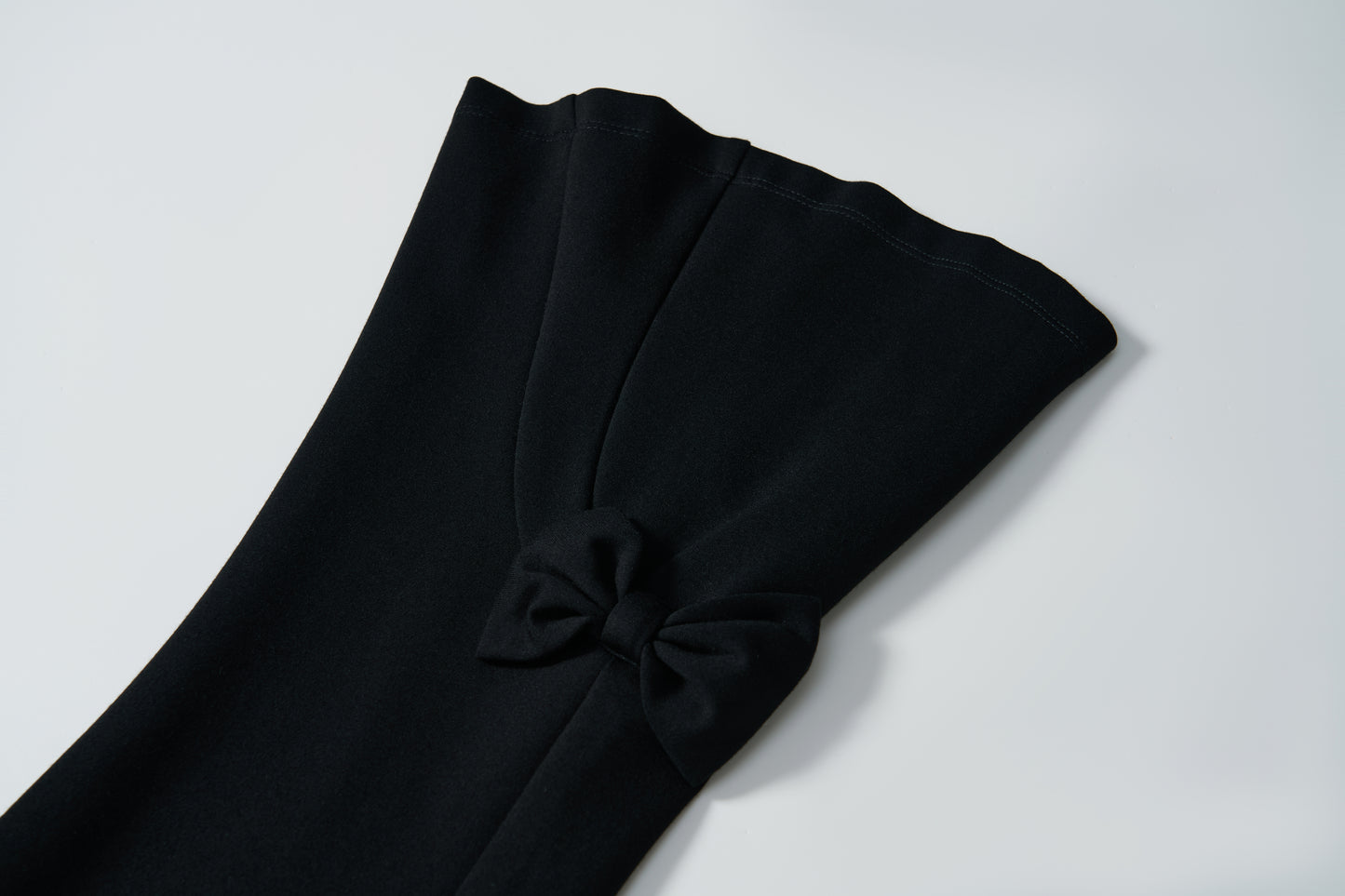Close-up of the black stretchy sleeve of KIKI and JOJO's Petal Whisper Dress Pants, featuring a small pleat and decorative bow near the cuff, set against a plain white background.