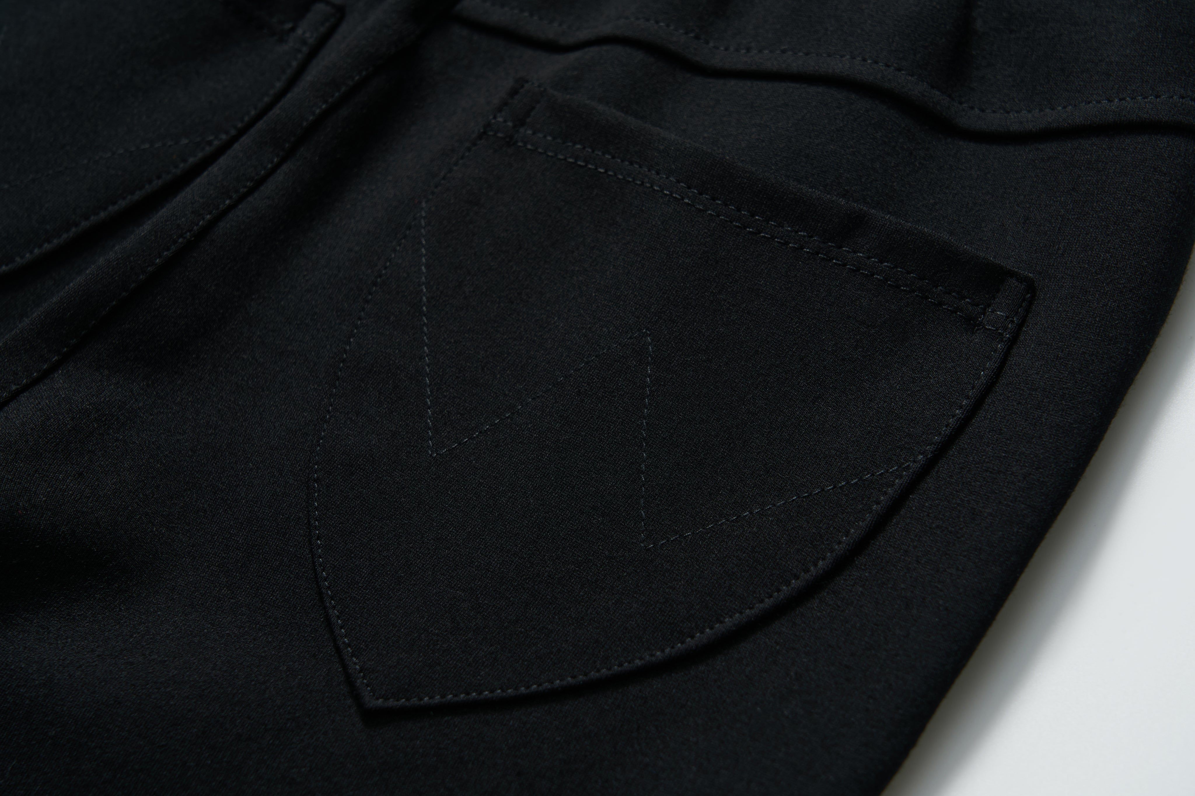 Close-up of a Petal Whisper Dress Pants pocket by KIKI and JOJO, featuring a black stretchy fabric with visible "W" pattern stitching on the flap.