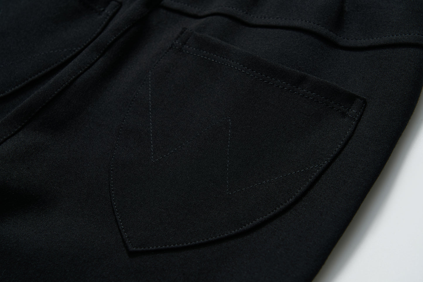 Close-up of a Petal Whisper Dress Pants pocket by KIKI and JOJO, featuring a black stretchy fabric with visible "W" pattern stitching on the flap.