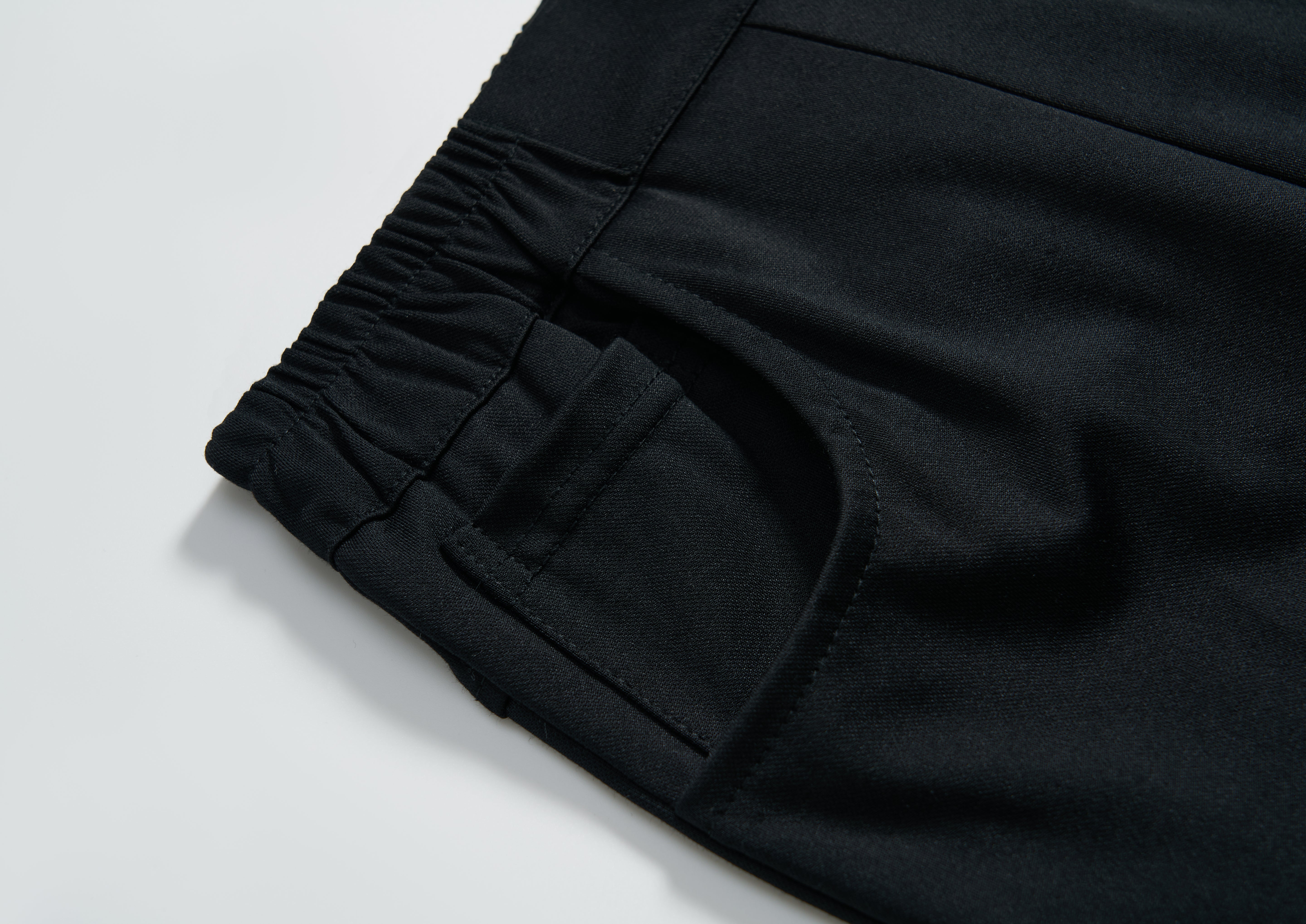 Close-up of the elastic waistband and pocket on KIKI and JOJO's Echo Whisper Dress Pants, showing off the smooth fabric, stitched seams, and flared black design.