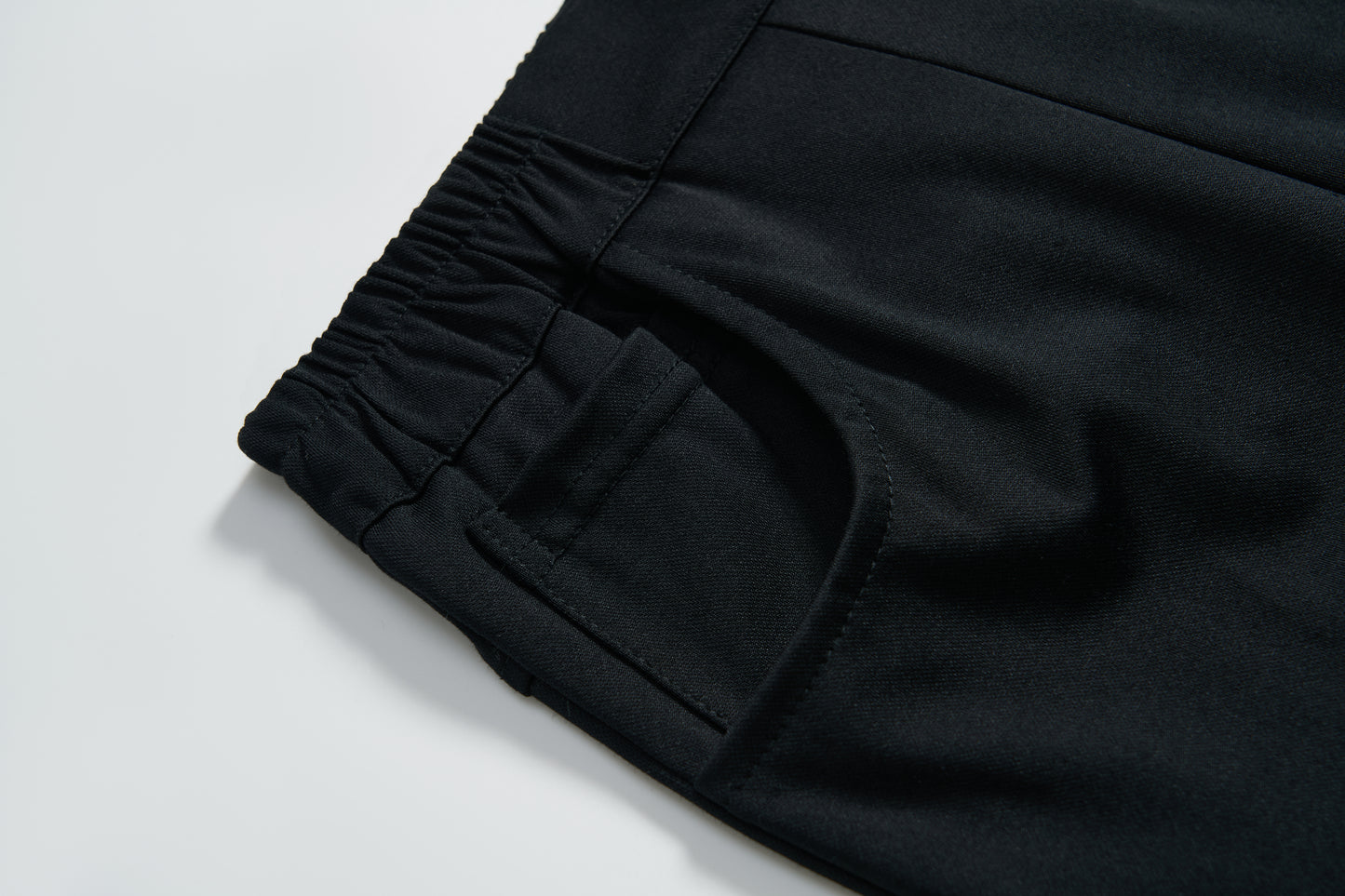 Close-up of the elastic waistband and pocket on KIKI and JOJO's Echo Whisper Dress Pants, showing off the smooth fabric, stitched seams, and flared black design.