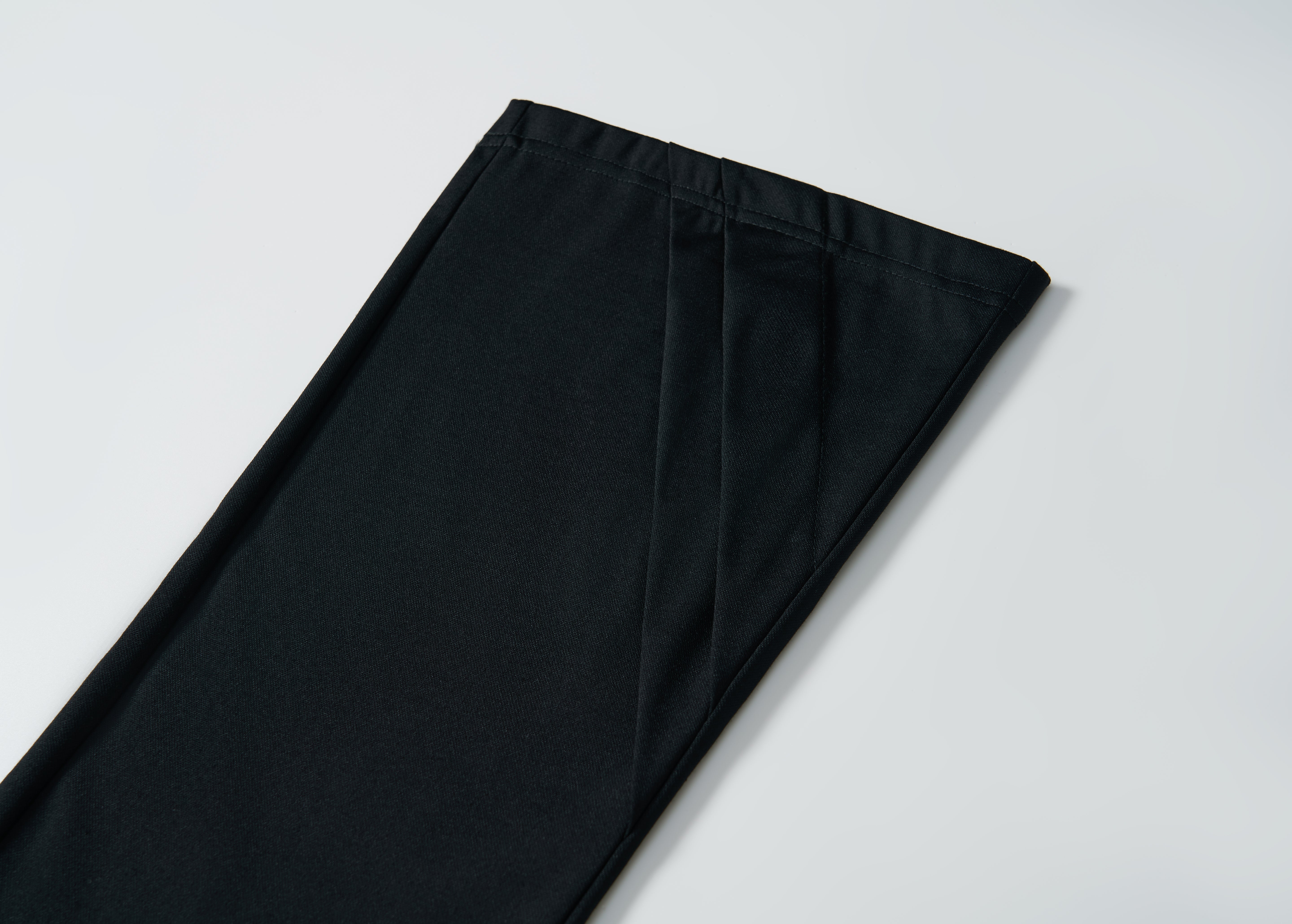 A close-up of the hem of KIKI and JOJO’s Echo Whisper Dress Pants in black, laid flat on a white surface, showcases their clean flared design.