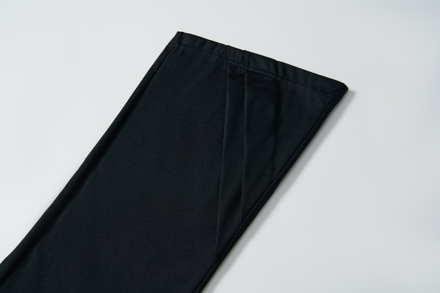 A close-up of the hem of KIKI and JOJO’s Echo Whisper Dress Pants in black, laid flat on a white surface, showcases their clean flared design.