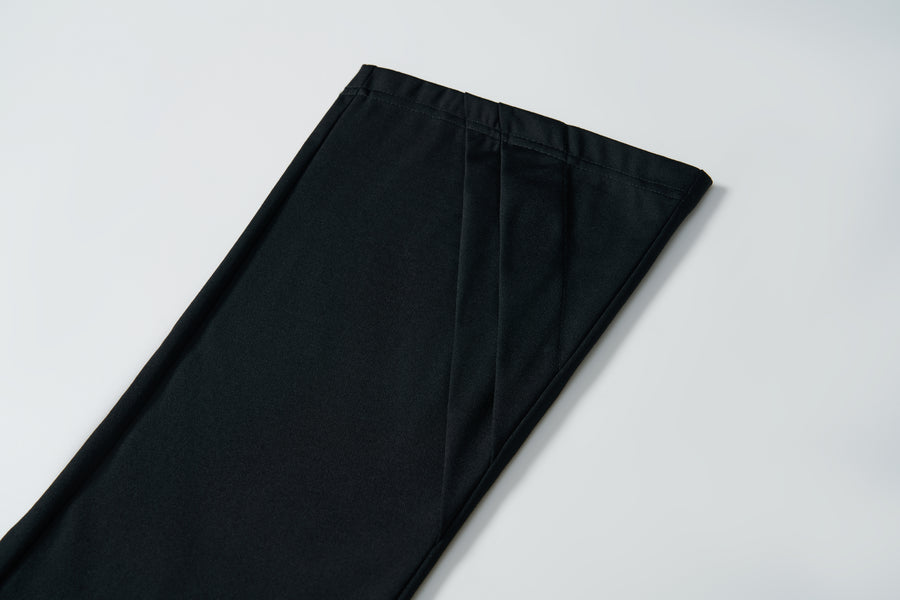 A close-up of the hem of KIKI and JOJO’s Echo Whisper Dress Pants in black, laid flat on a white surface, showcases their clean flared design.