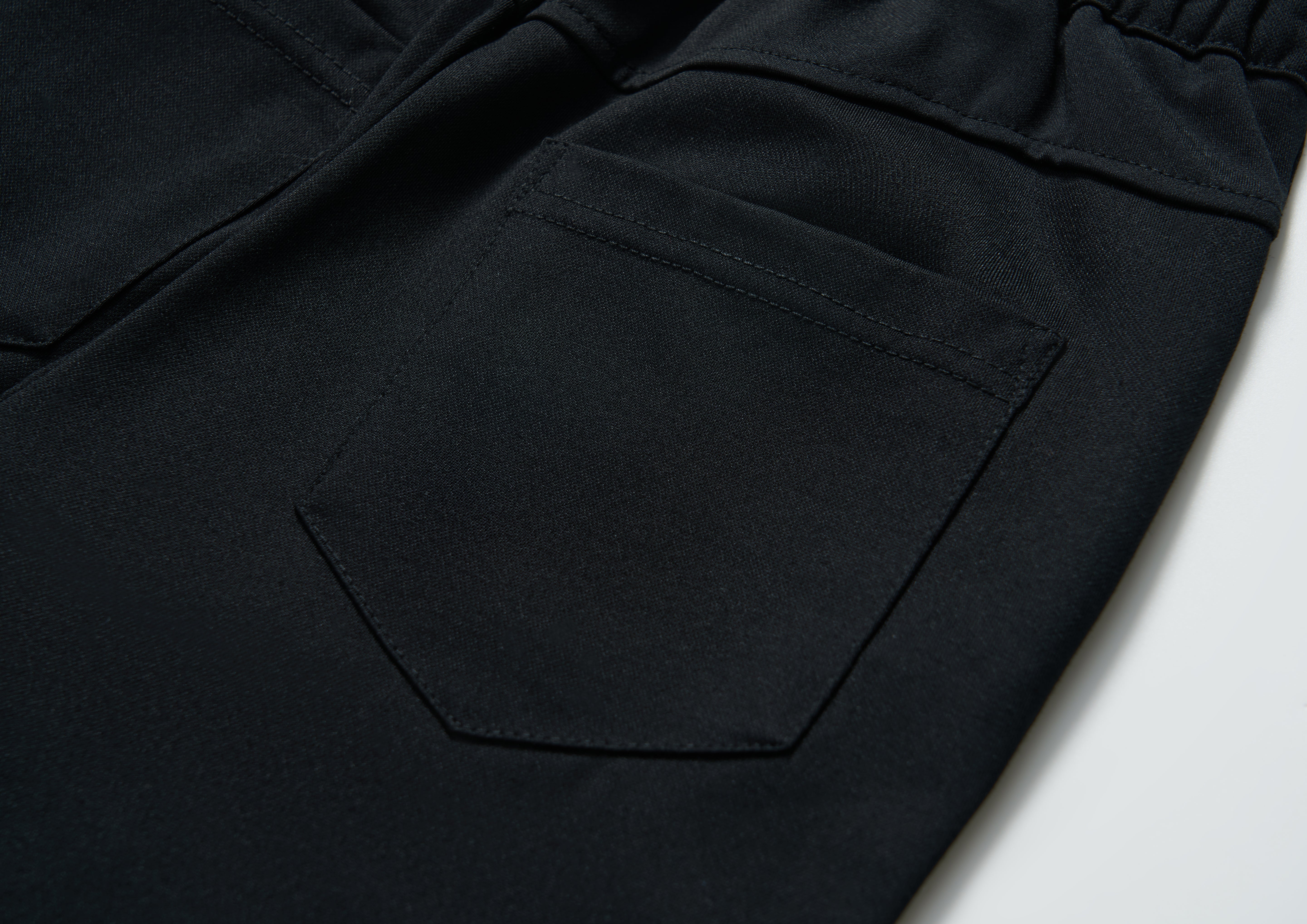 Close-up of the back pocket on KIKI and JOJO Echo Whisper Dress Pants, featuring detailed stitching and an elastic waistband on these flared black pants.