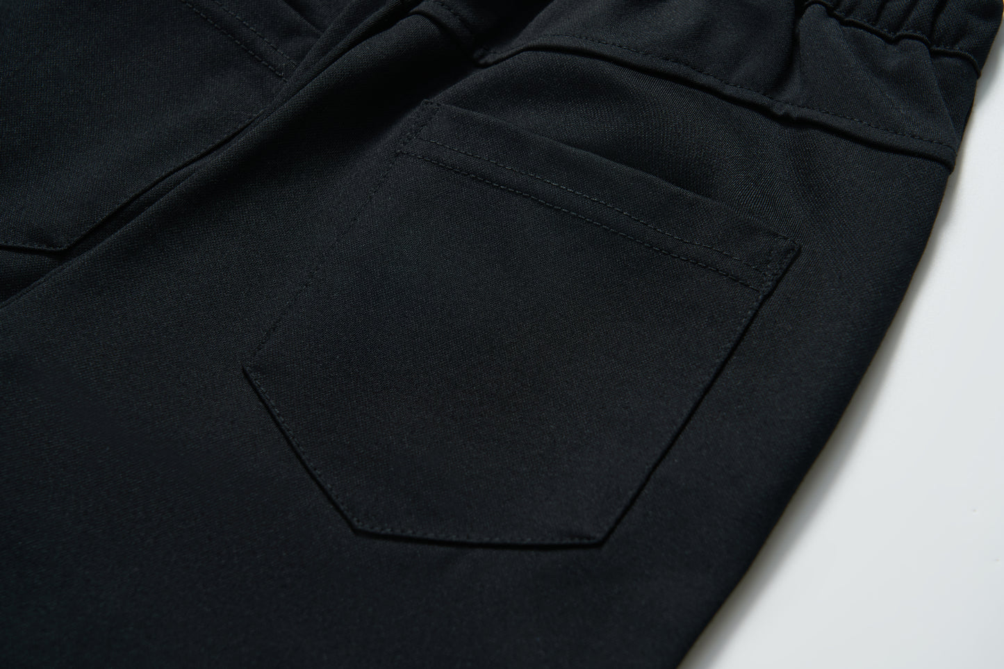 Close-up of the back pocket on KIKI and JOJO Echo Whisper Dress Pants, featuring detailed stitching and an elastic waistband on these flared black pants.