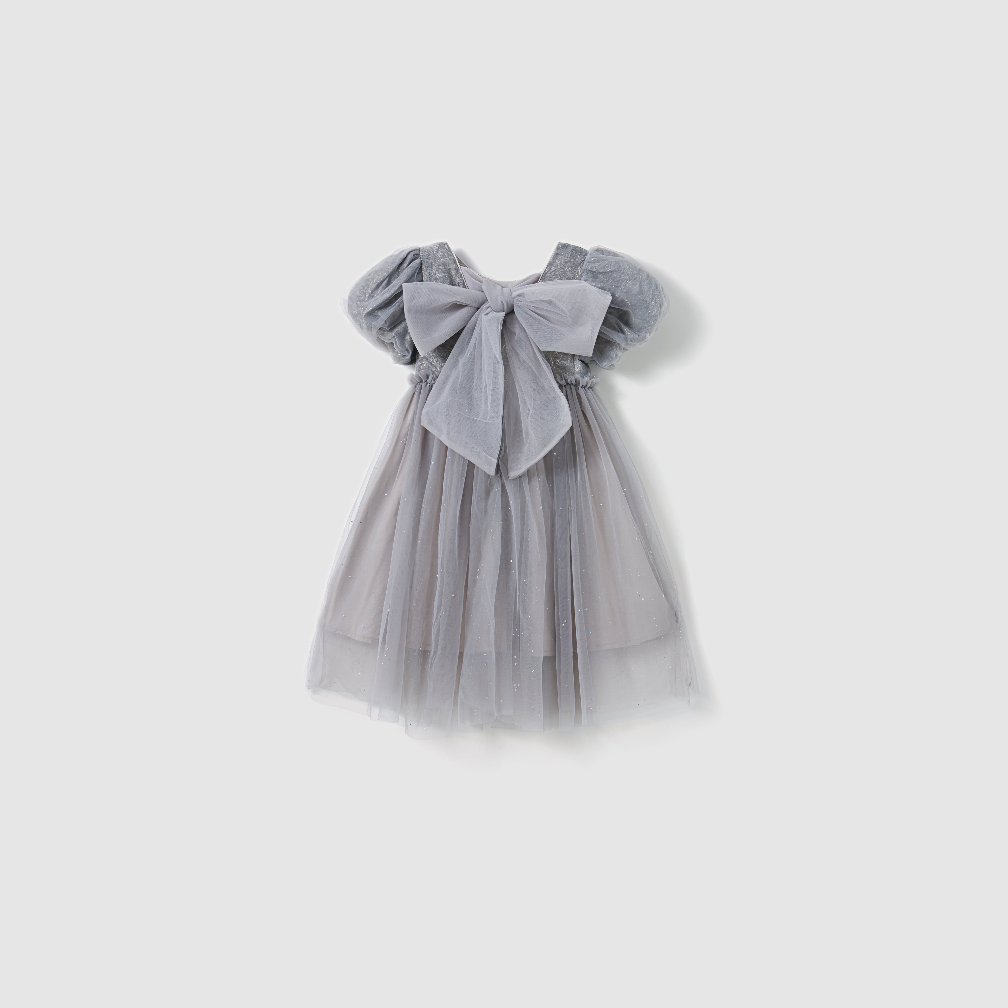 The KIKI and JOJO Dusk Whisper Dress is a glittering gray tulle dress with short puff sleeves and a large front bow, shown against a plain white background.