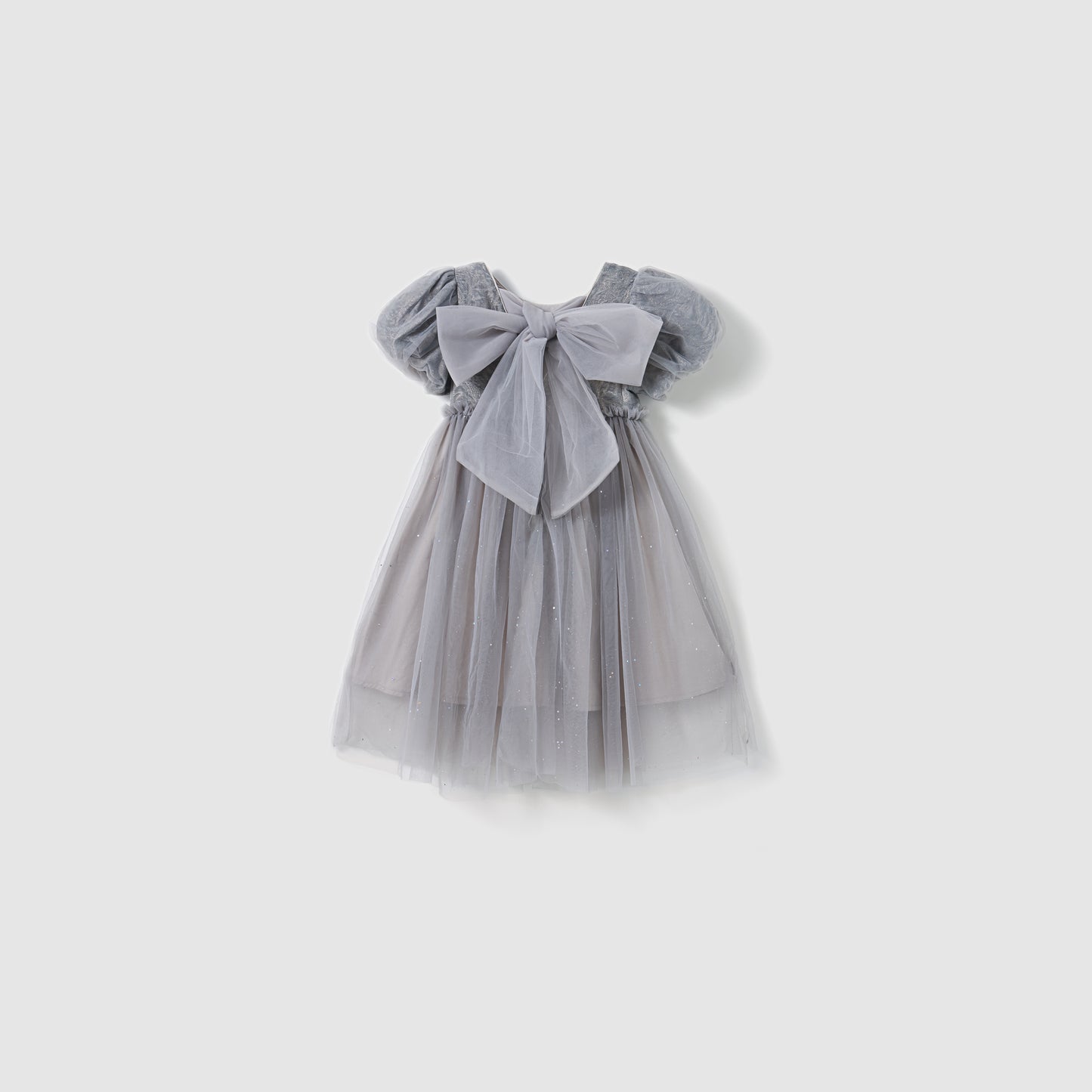 The KIKI and JOJO Dusk Whisper Dress is a glittering gray tulle dress with short puff sleeves and a large front bow, shown against a plain white background.