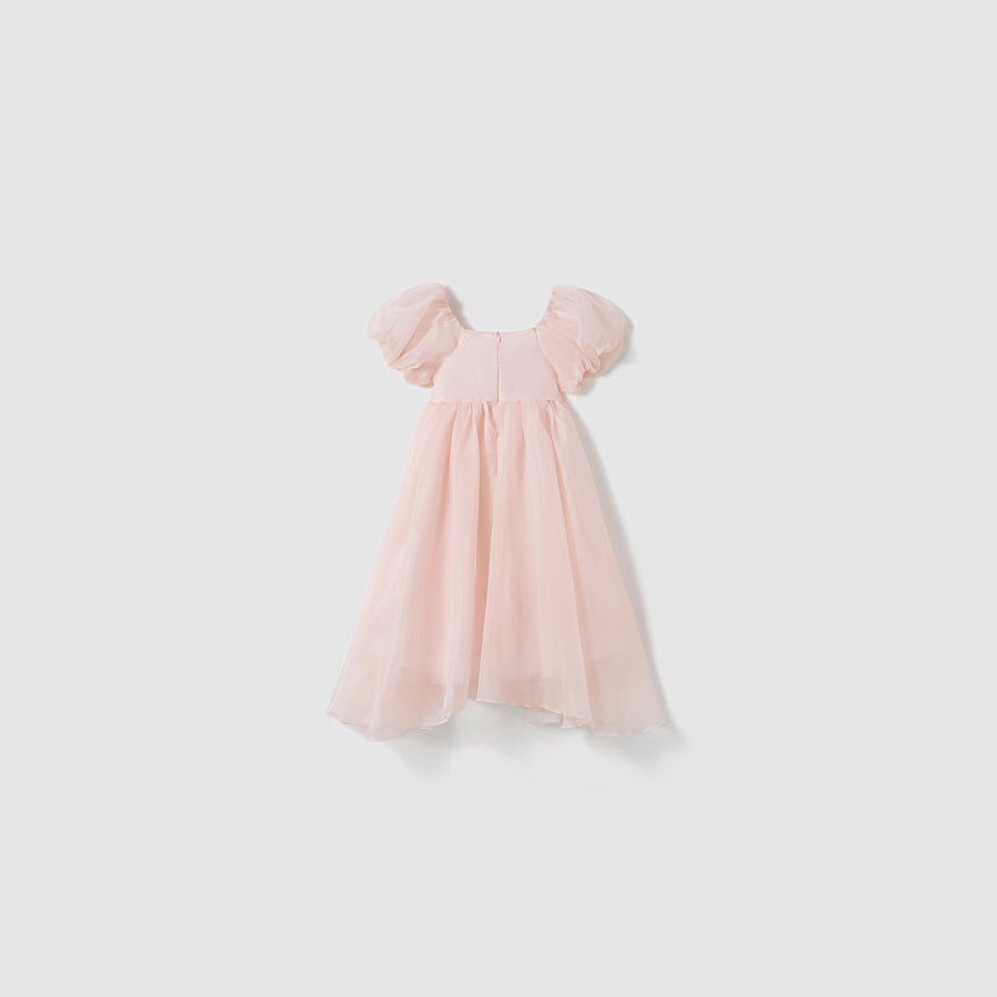 The Blush Whisper Dress by KIKI and JOJO is a light pink, ankle-length, princess-style dress with short puff sleeves, a flowing skirt, and delicate 3D floral appliqués, shown on a plain white background.
