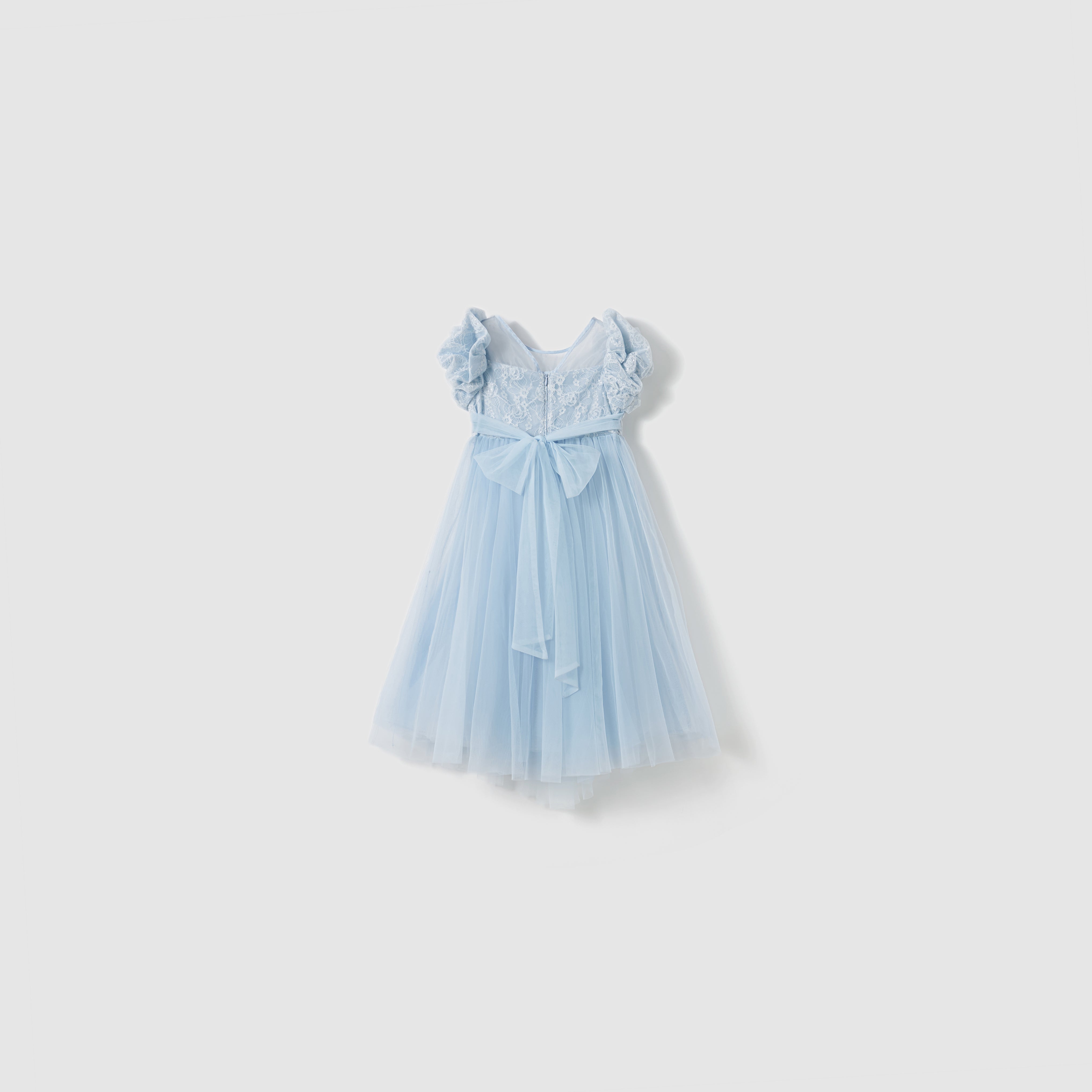 The Sky Whisper Dress by KIKI and JOJO is a light blue, knee-length organza dress featuring short ruffled sleeves, a lace bodice, and a large bow at the waist, shown on a plain white background.
