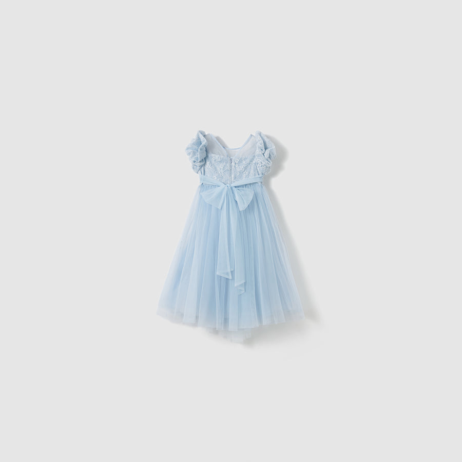 The Sky Whisper Dress by KIKI and JOJO is a light blue, knee-length organza dress featuring short ruffled sleeves, a lace bodice, and a large bow at the waist, shown on a plain white background.