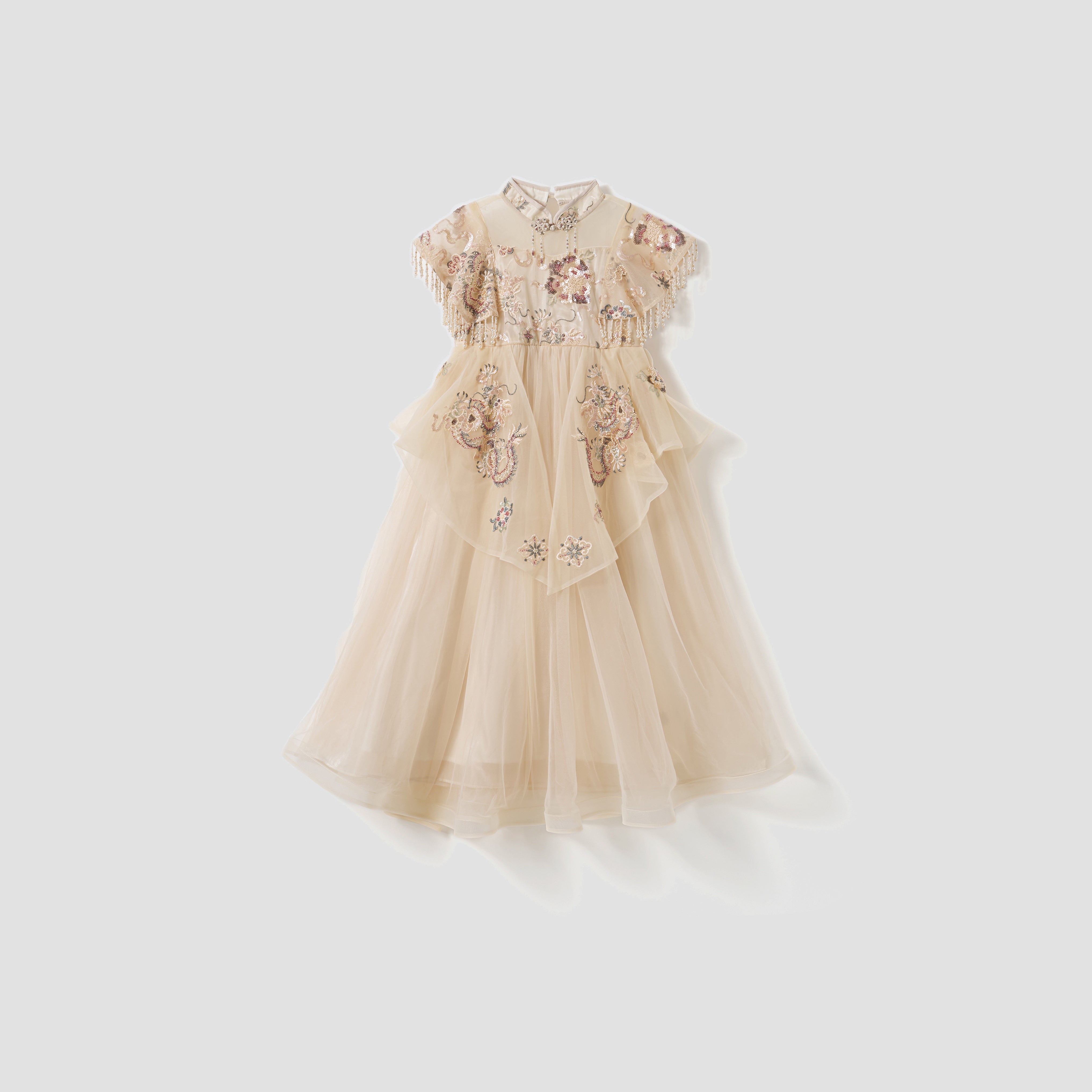 The KIKI and JOJO Jade Whisper Dress is a beige, short-sleeved girls’ cheongsam with a layered design, embroidered florals, and bead embellishments, shown against a plain light background.