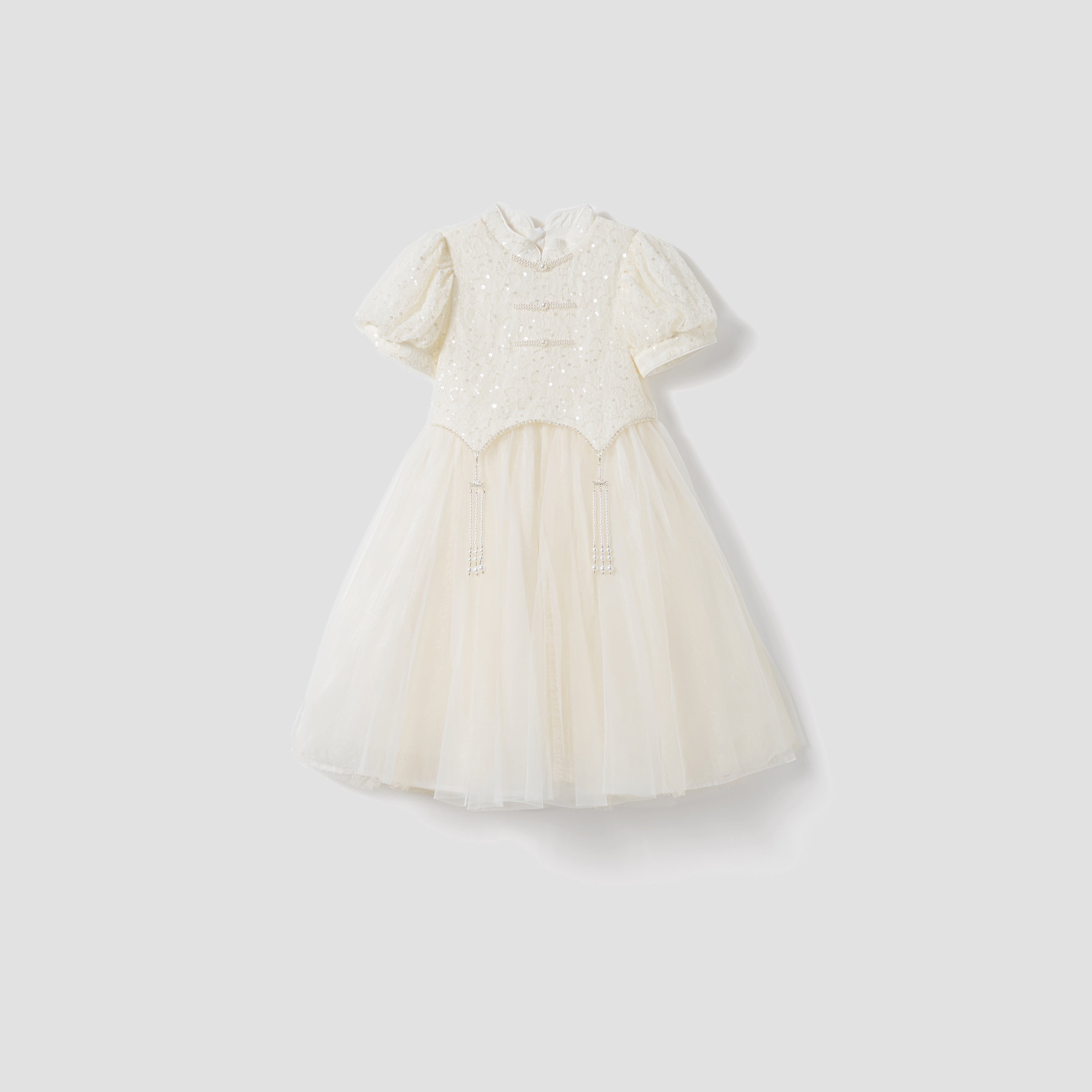 The Orchid Whisper Dress by KIKI and JOJO is a white, short-sleeved, knee-length modern vintage dress with a sequin-embroidered lace bodice, decorative buttons, and a tulle skirt, shown on a light gray background.