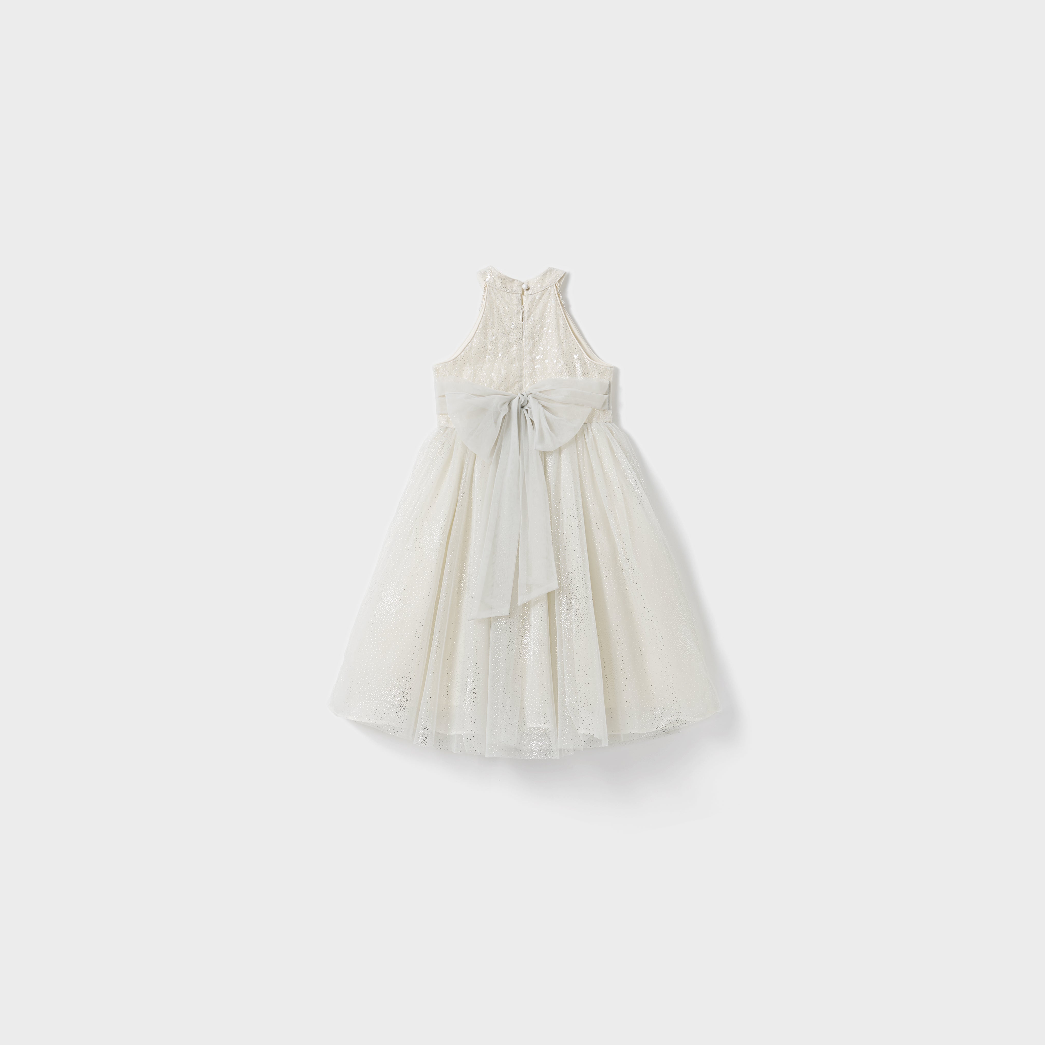 The Gilded Whisper Dress by KIKI and JOJO is a sleeveless white lace children's dress, featuring a large light gray back bow. Its classic beaded tassel-inspired design is beautifully displayed against a plain white background.
