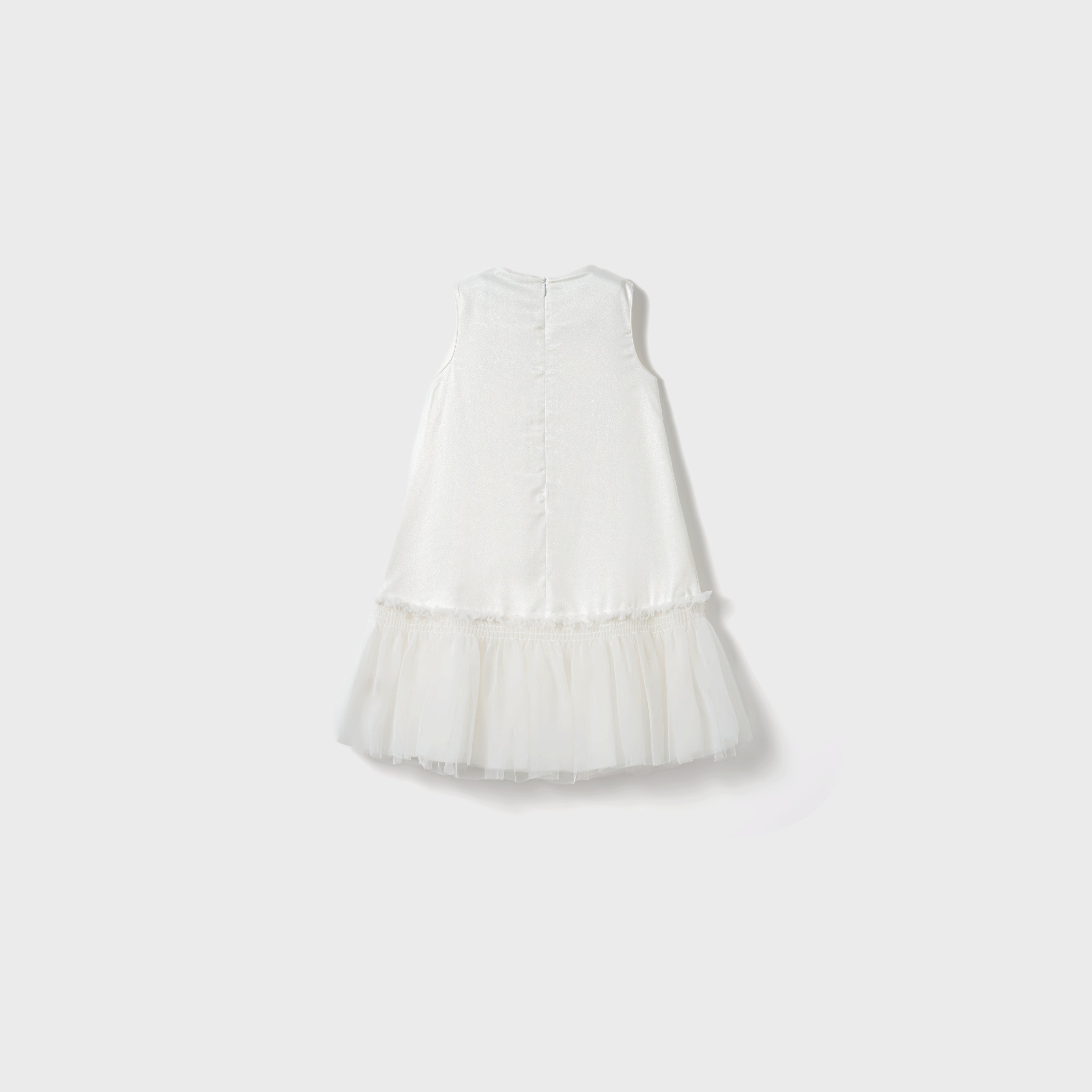The Twinkle Whisper Dress by KIKI and JOJO is a sleeveless white A-line children’s dress with a tulle skirt, button-back closure, and embroidered lace details, shown against a simple light background.
