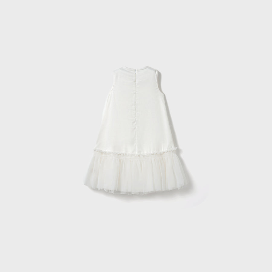 The Twinkle Whisper Dress by KIKI and JOJO is a sleeveless white A-line children’s dress with a tulle skirt, button-back closure, and embroidered lace details, shown against a simple light background.