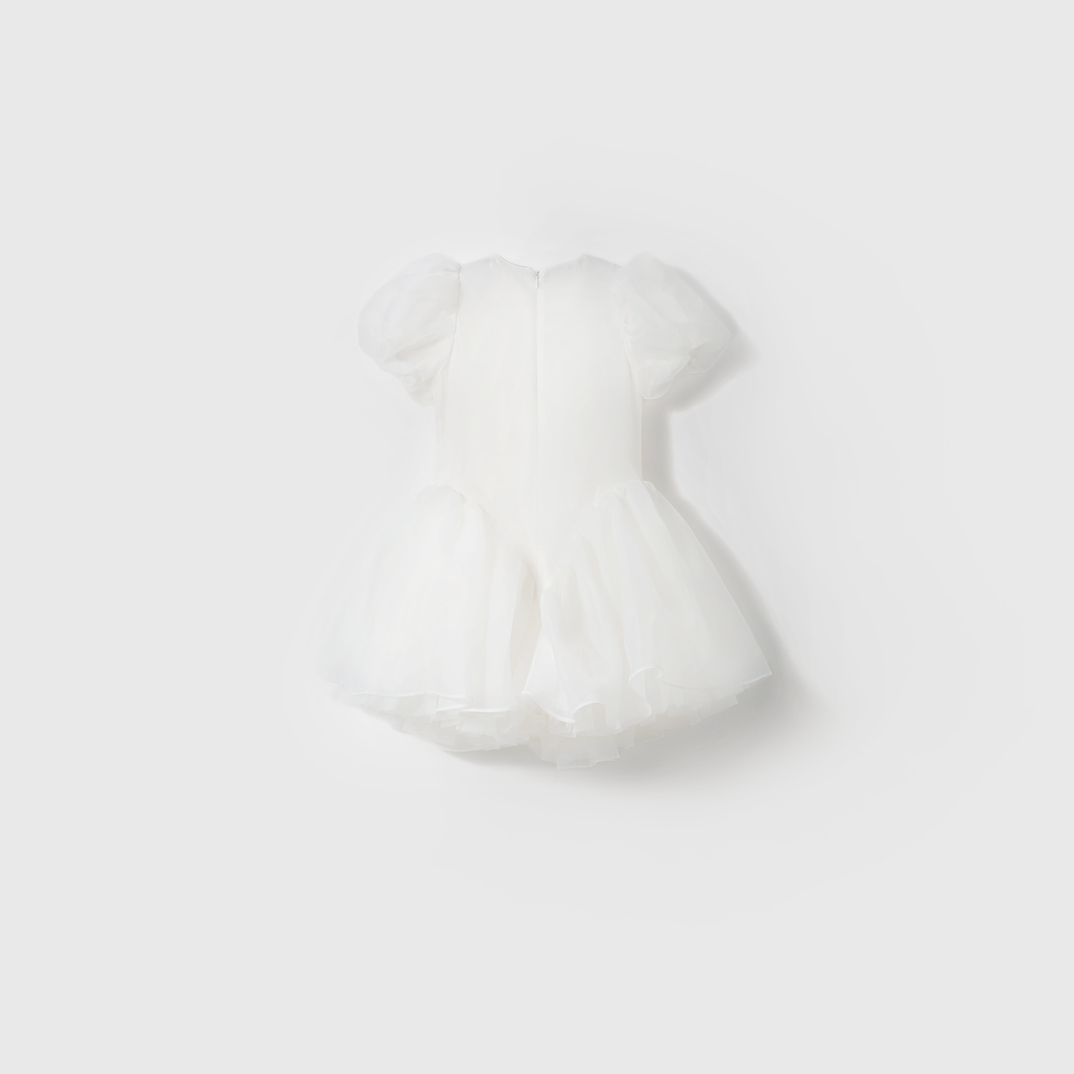 The Ballerina Whisper Dress by KIKI and JOJO is a white mini dress featuring short puffed sleeves, tulle fabric, and a flared skirt, showcased against a plain light background.