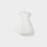 The Whisper Bloom Dress by KIKI and JOJO is a white, knee-length mini dress with short sleeves, floral embroidery, a tulle overlay, and subtle bead accents, shown against a plain light background.