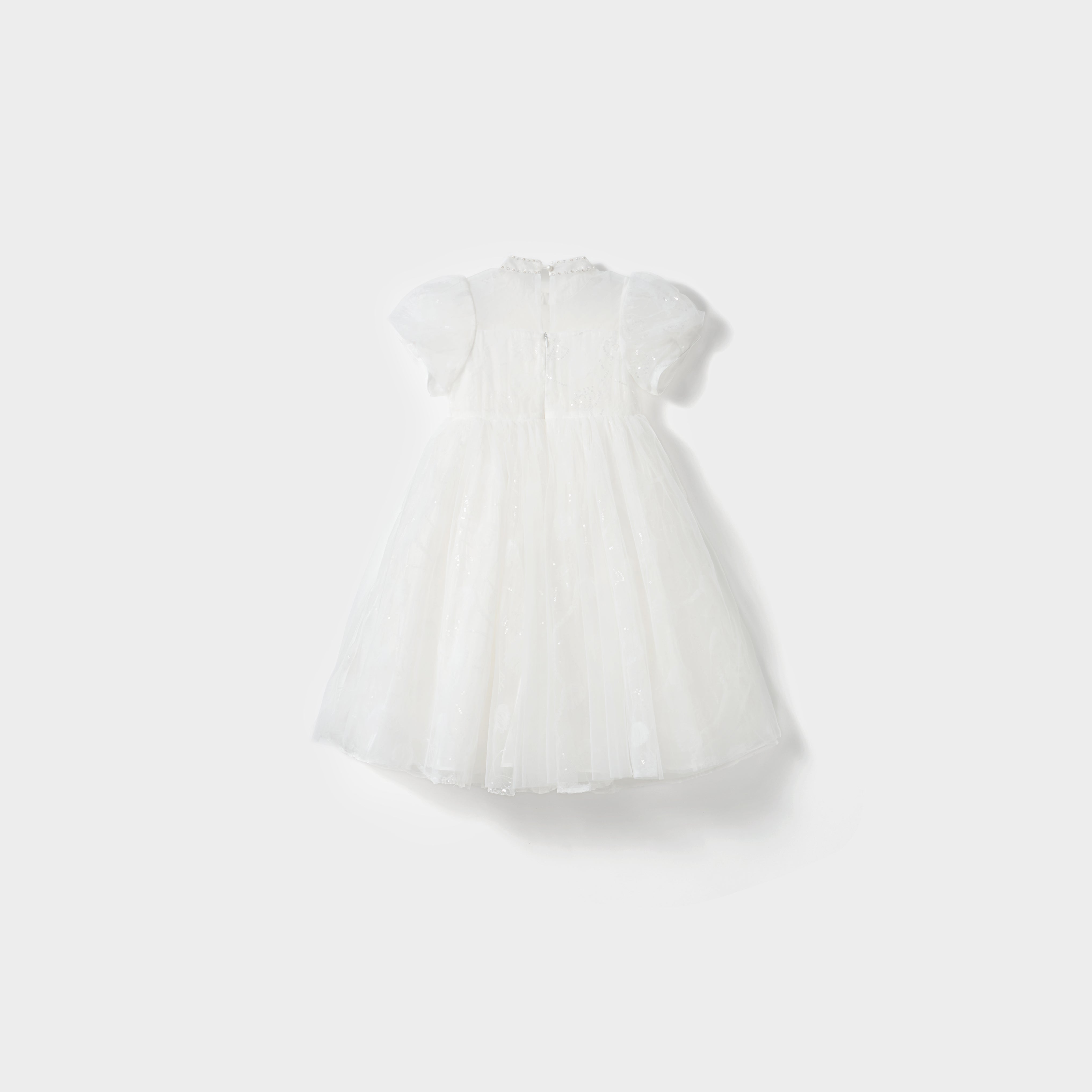 The Whisper Bloom Dress by KIKI and JOJO is a white, knee-length mini dress with short sleeves, floral embroidery, a tulle overlay, and subtle bead accents, shown against a plain light background.