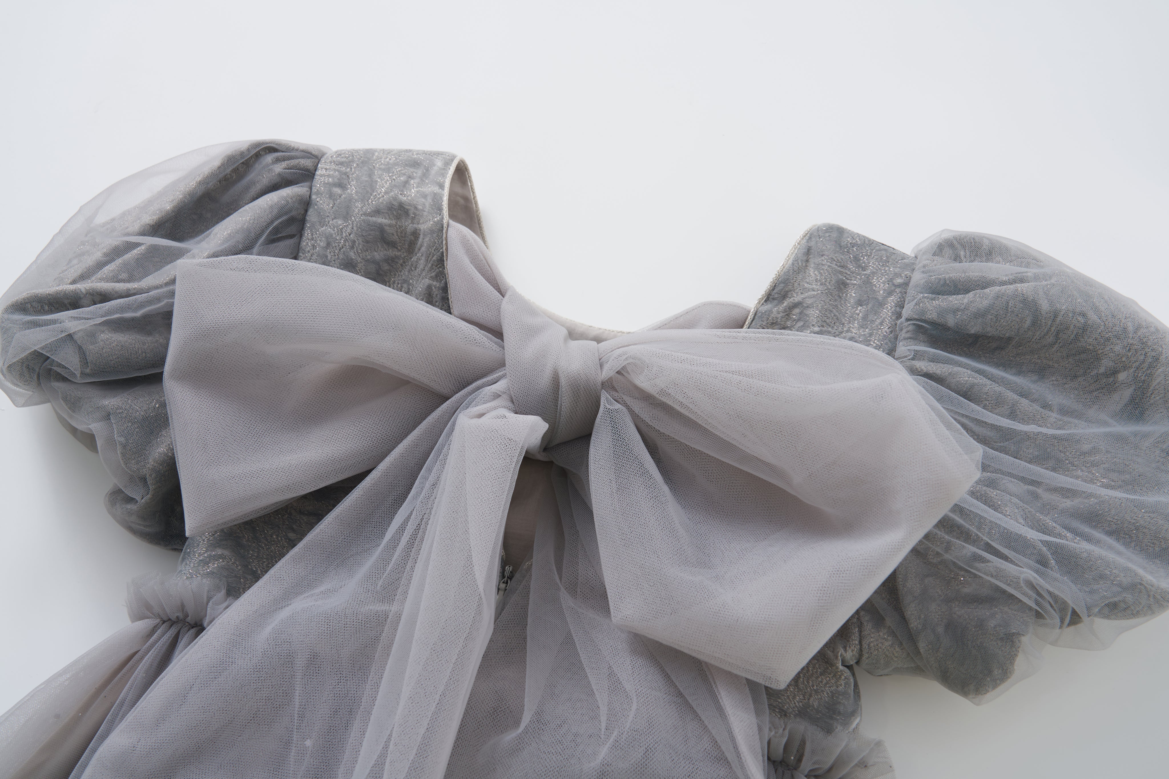 Close-up of a light gray sheer fabric bow on puffed sleeves, part of the elegant Dusk Whisper Dress by KIKI and JOJO, displayed against a plain white background.