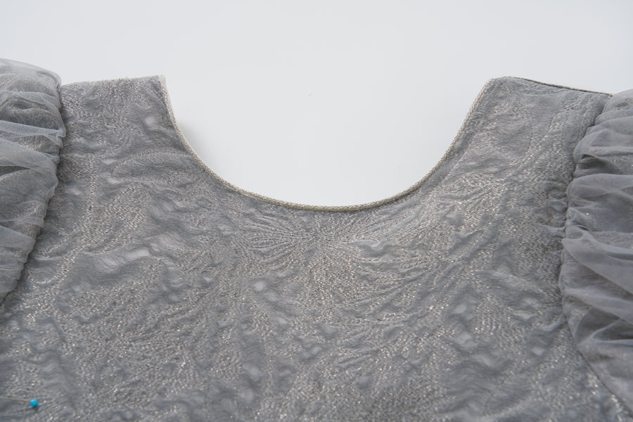 Close-up of the Dusk Whisper Dress by KIKI and JOJO, showcasing its textured grey fabric, tulle puff sleeves, and rounded neckline against a plain white background.