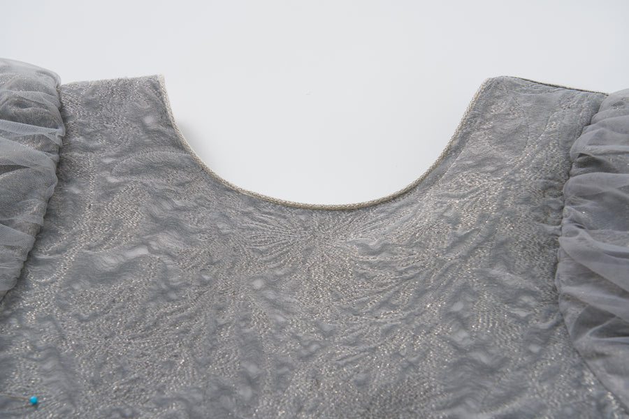 Close-up of the Dusk Whisper Dress by KIKI and JOJO, featuring a grey puff-sleeve design with a scoop neckline and sheer ruffled sleeves, displayed on a white background.