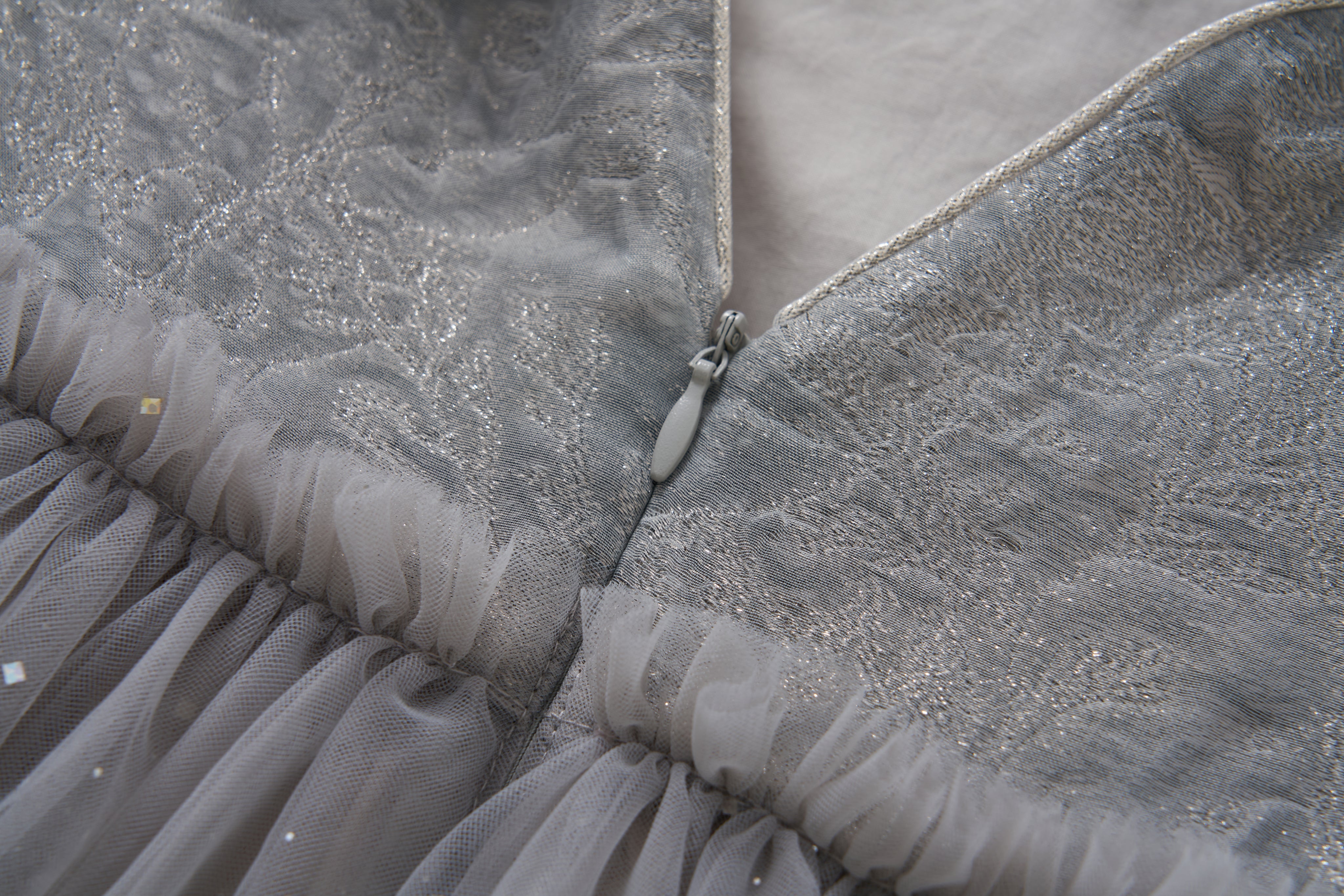 Close-up of the Dusk Whisper Dress by KIKI and JOJO, showcasing glittering silver tulle fabric, delicate tulle ruffles, and a partially unzipped silver zipper at the back.