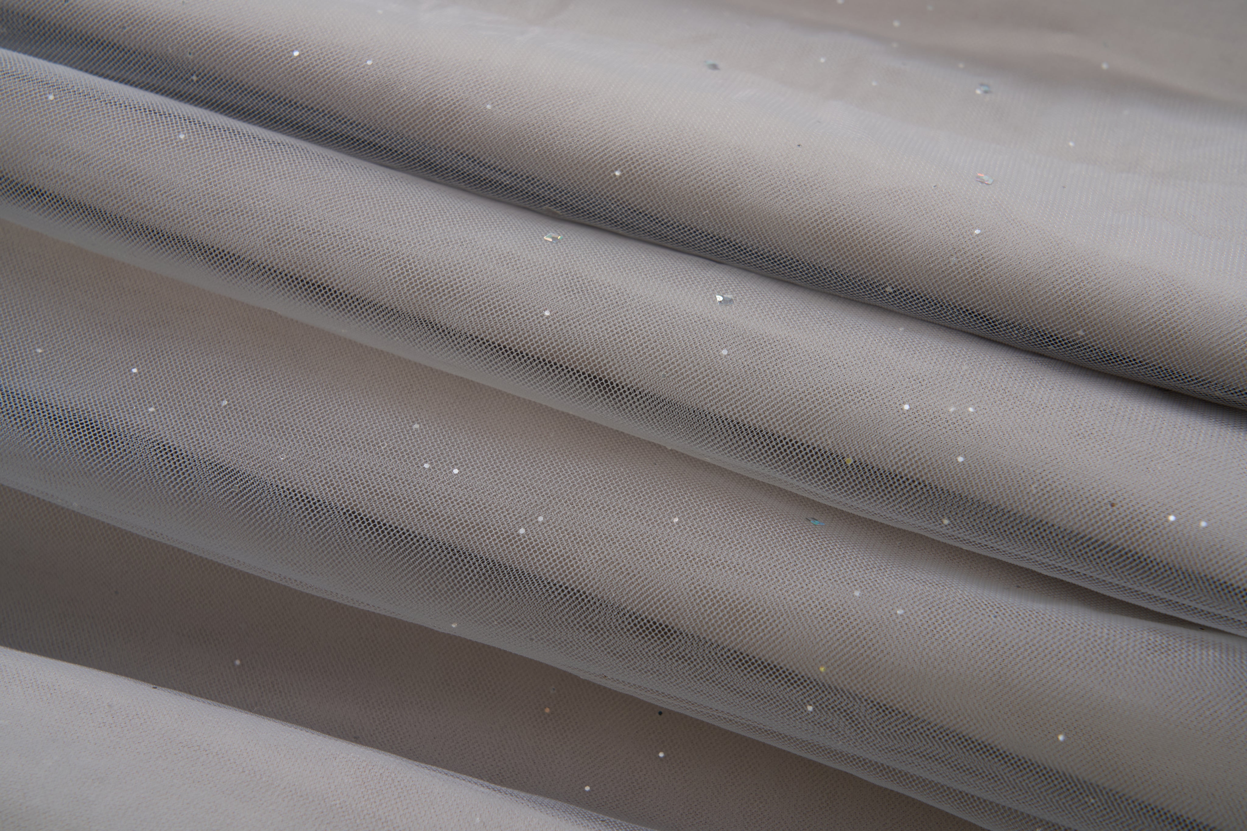 Close-up of the Dusk Whisper Dress by KIKI and JOJO: light gray sheer mesh fabric with scattered shiny sequins, elegantly draped—ideal for a glittering tulle look or a stylish grey puff-sleeve dress.