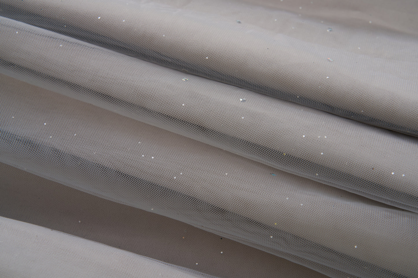 Close-up of the Dusk Whisper Dress by KIKI and JOJO: light gray sheer mesh fabric with scattered shiny sequins, elegantly draped—ideal for a glittering tulle look or a stylish grey puff-sleeve dress.