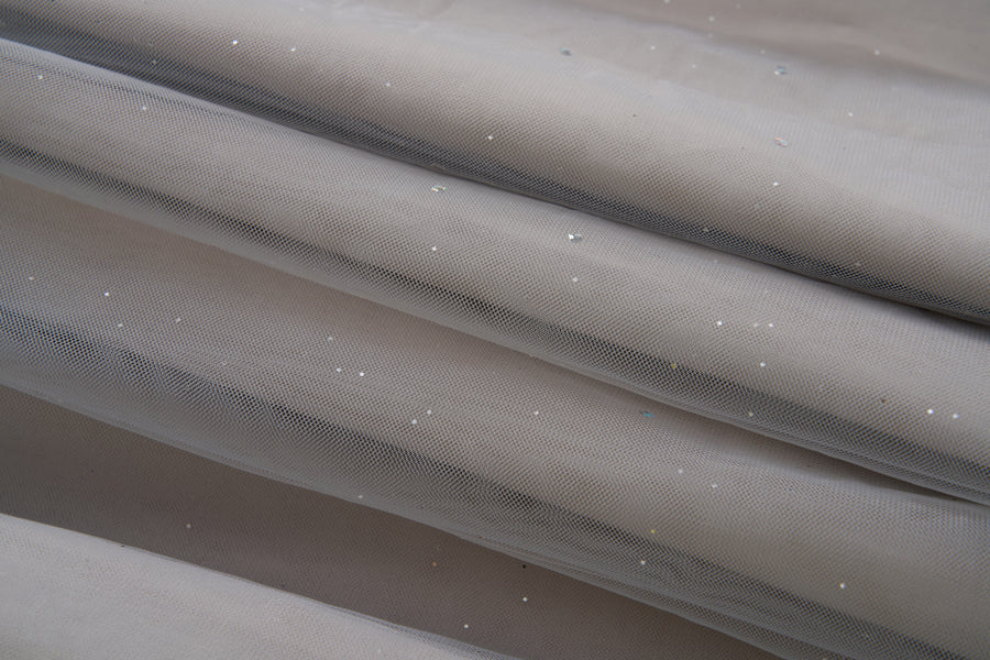 Close-up of the Dusk Whisper Dress by KIKI and JOJO: light gray sheer mesh fabric with scattered shiny sequins, elegantly draped—ideal for a glittering tulle look or a stylish grey puff-sleeve dress.
