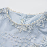Close-up of the Mist Whisper Dress by KIKI and JOJO—an A-line light blue dress with hand-embroidered florals, sequins, sheer tulle sleeves, and a neckline finished with a delicate pearl trim.