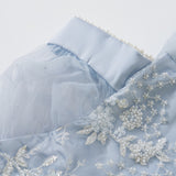 Close-up of the Mist Whisper Dress by KIKI and JOJO in pale blue, featuring pearl trim, sheer puff sleeves, and delicate hand-embroidered floral details with sequins and beads.