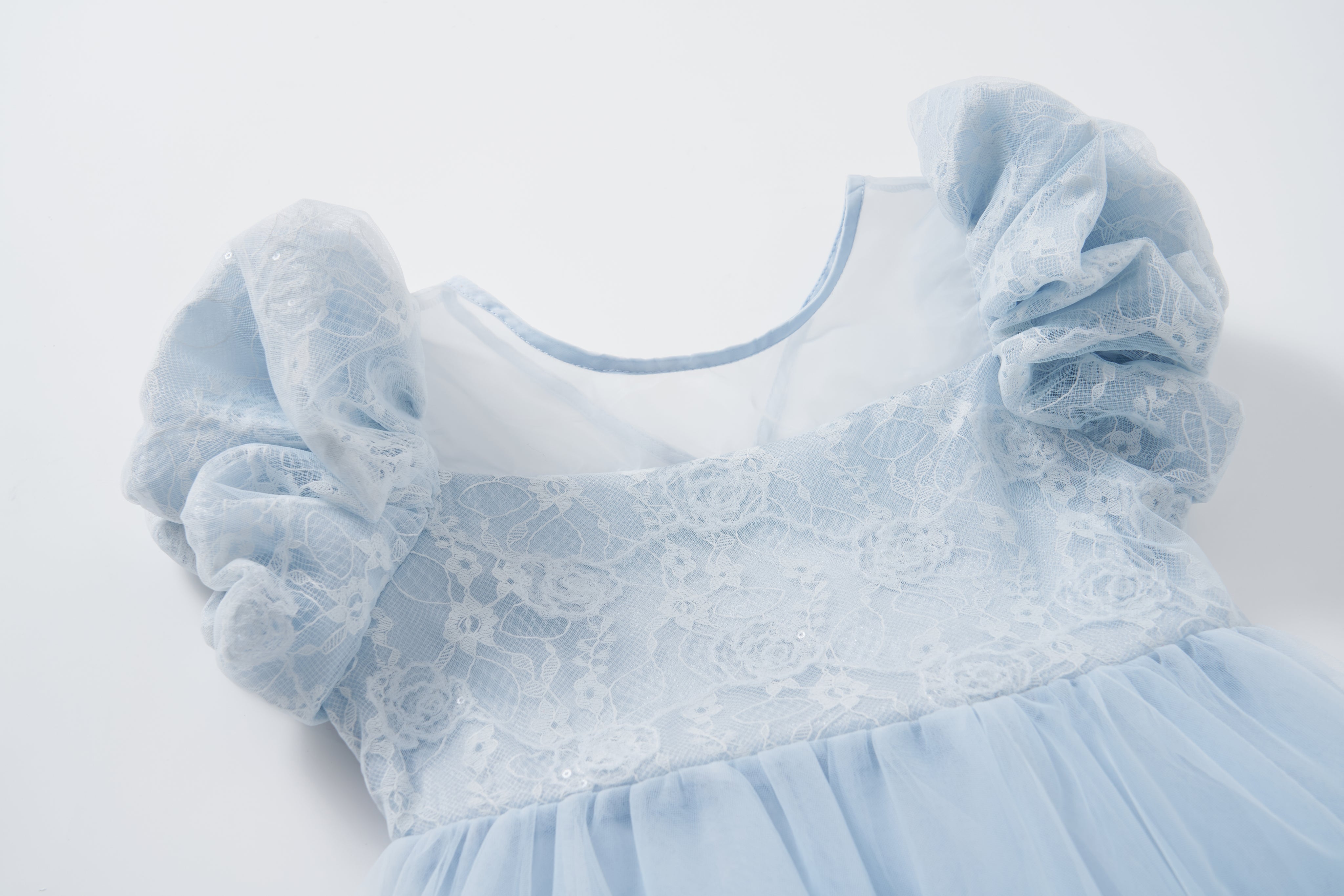 The Sky Whisper Dress by KIKI and JOJO features puffed lace sleeves, a lace overlay bodice, and a flowing tulle skirt in light blue, displayed on a white background.