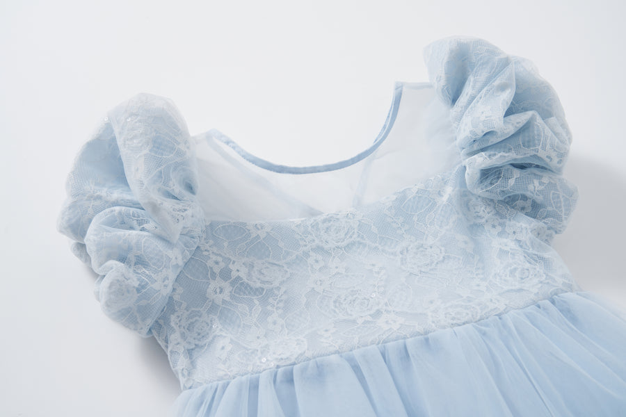 The Sky Whisper Dress by KIKI and JOJO features puffed lace sleeves, a lace overlay bodice, and a flowing tulle skirt in light blue, displayed on a white background.
