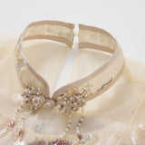 Close-up of the Jade Whisper Dress by KIKI and JOJO, a traditional cream cheongsam featuring a sheer mandarin collar, embroidered florals, sequins, and beaded neckline accents.