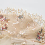Close-up of the Jade Whisper Dress by KIKI and JOJO: beige fabric with embroidered florals, sequin details, and pearl bead fringe—perfect for an elegant cheongsam—shown on a white background.