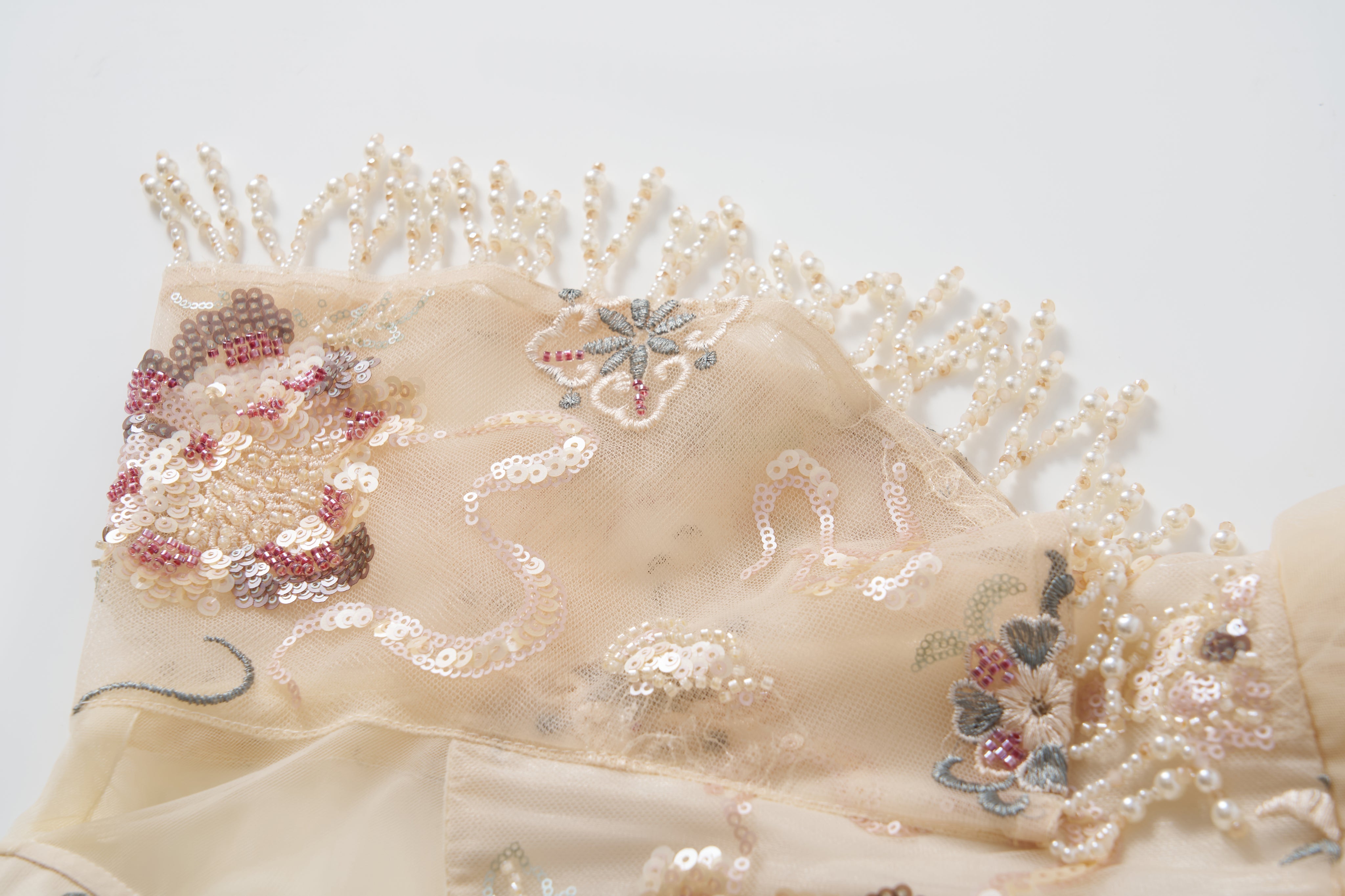 Close-up of the Jade Whisper Dress by KIKI and JOJO: beige fabric with embroidered florals, sequin details, and pearl bead fringe—perfect for an elegant cheongsam—shown on a white background.