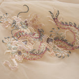 A close-up of the Jade Whisper Dress by KIKI and JOJO, showcasing its light-toned cheongsam fabric adorned with an intricate dragon motif embroidered in sequins, beads, and soft pastel hues.