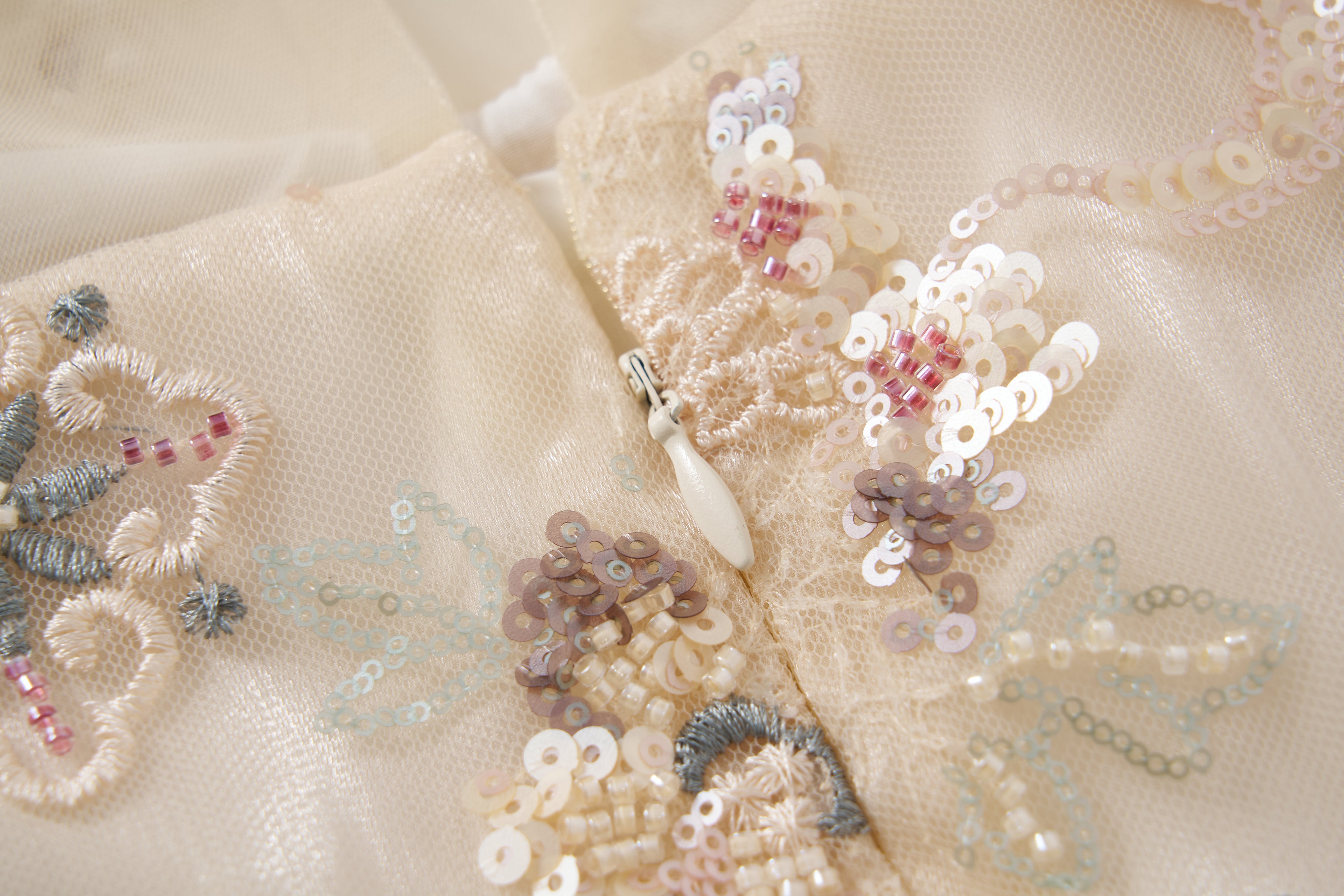 Close-up of the Jade Whisper Dress by KIKI and JOJO, featuring cream fabric adorned with embroidered florals, sequins, beads, and a small white zipper—reflecting cheongsam-inspired elegance.