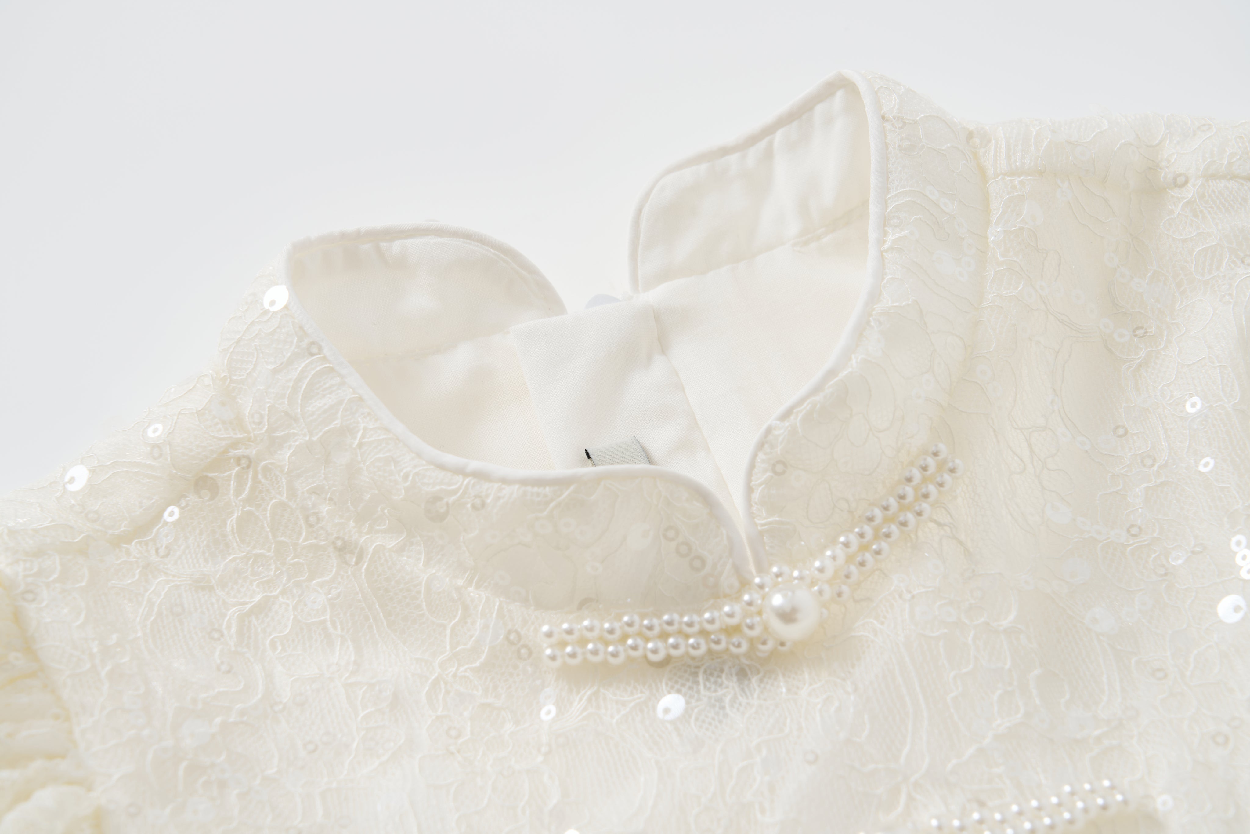 Close-up of the Orchid Whisper Dress by KIKI and JOJO, highlighting its sequin embroidered lace, pearl embellishments, and high collar against a white background.