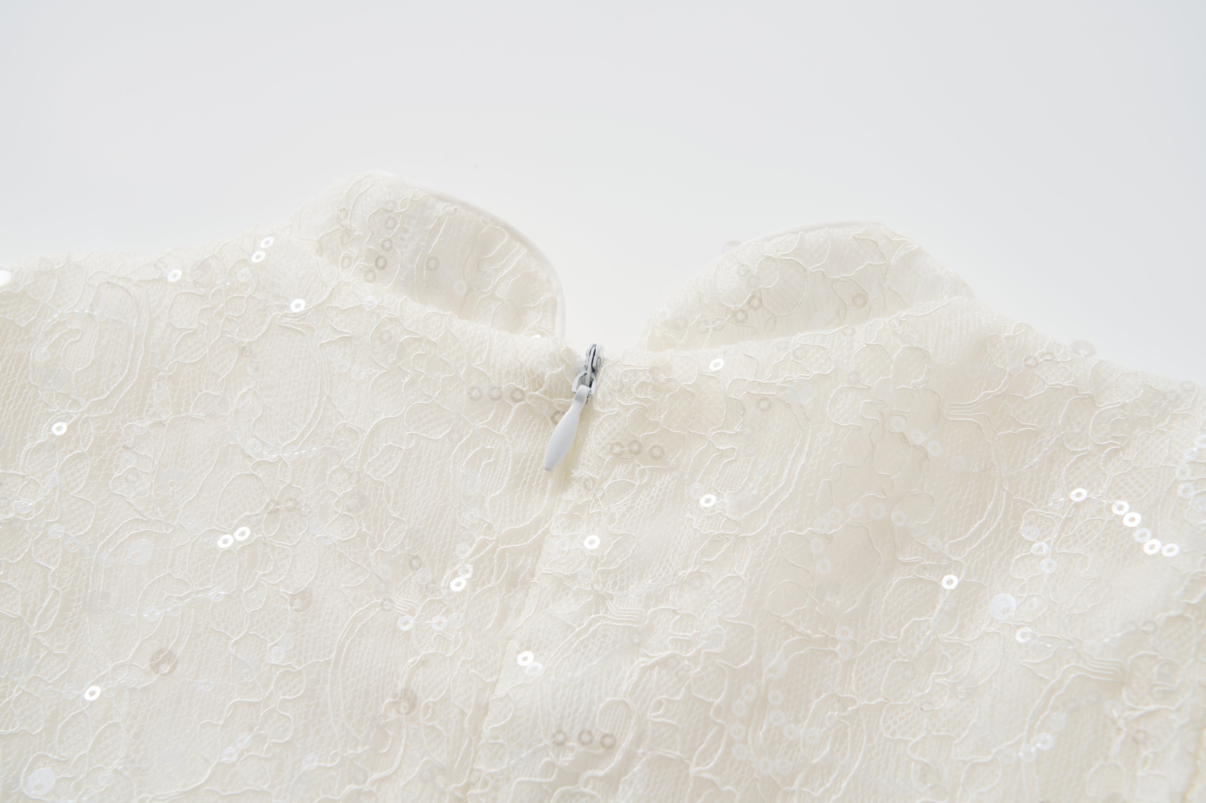 Close-up of the back of KIKI and JOJO's Orchid Whisper Dress, a cream-colored cheongsam with sequin-embroidered lace and a partially fastened visible zipper at the neckline.