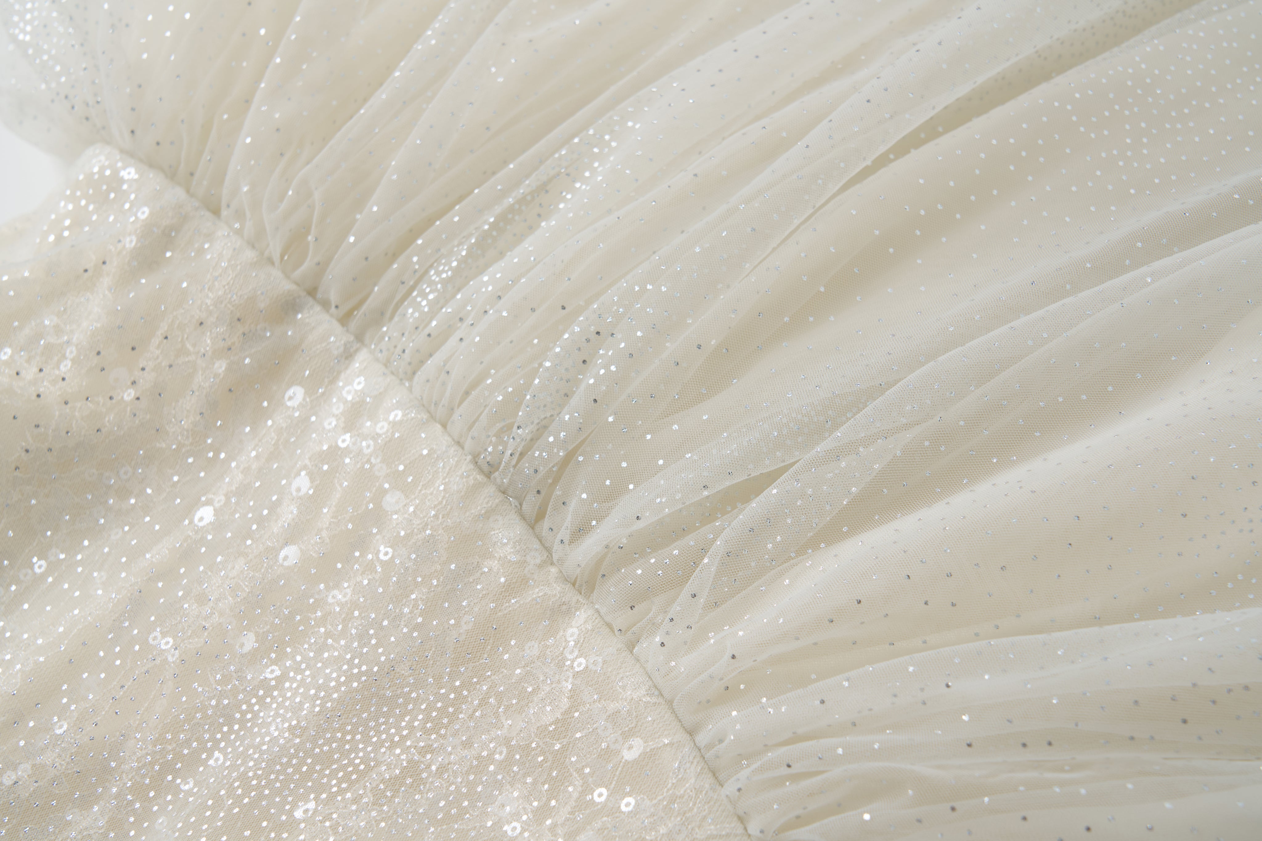 Close-up of the Gilded Whisper Dress by KIKI and JOJO—a beige tulle dress with a sheer overlay, adorned with sequins, small sparkling dots, and gathered stitching.