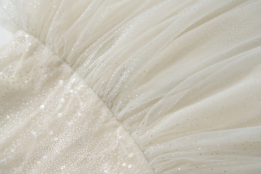 Close-up of the Gilded Whisper Dress by KIKI and JOJO—a beige tulle dress with a sheer overlay, adorned with sequins, small sparkling dots, and gathered stitching.
