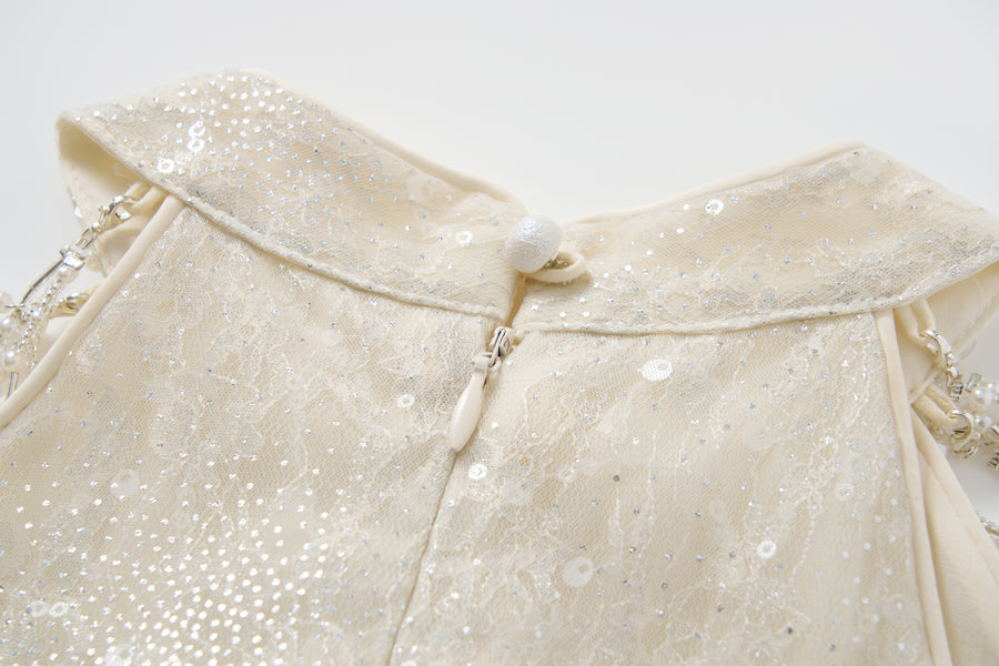 Close-up of the back of the KIKI and JOJO Gilded Whisper Dress: a cream halter-neck sequin dress with lace fabric, zipper, fabric-covered button, and beaded shoulder straps.