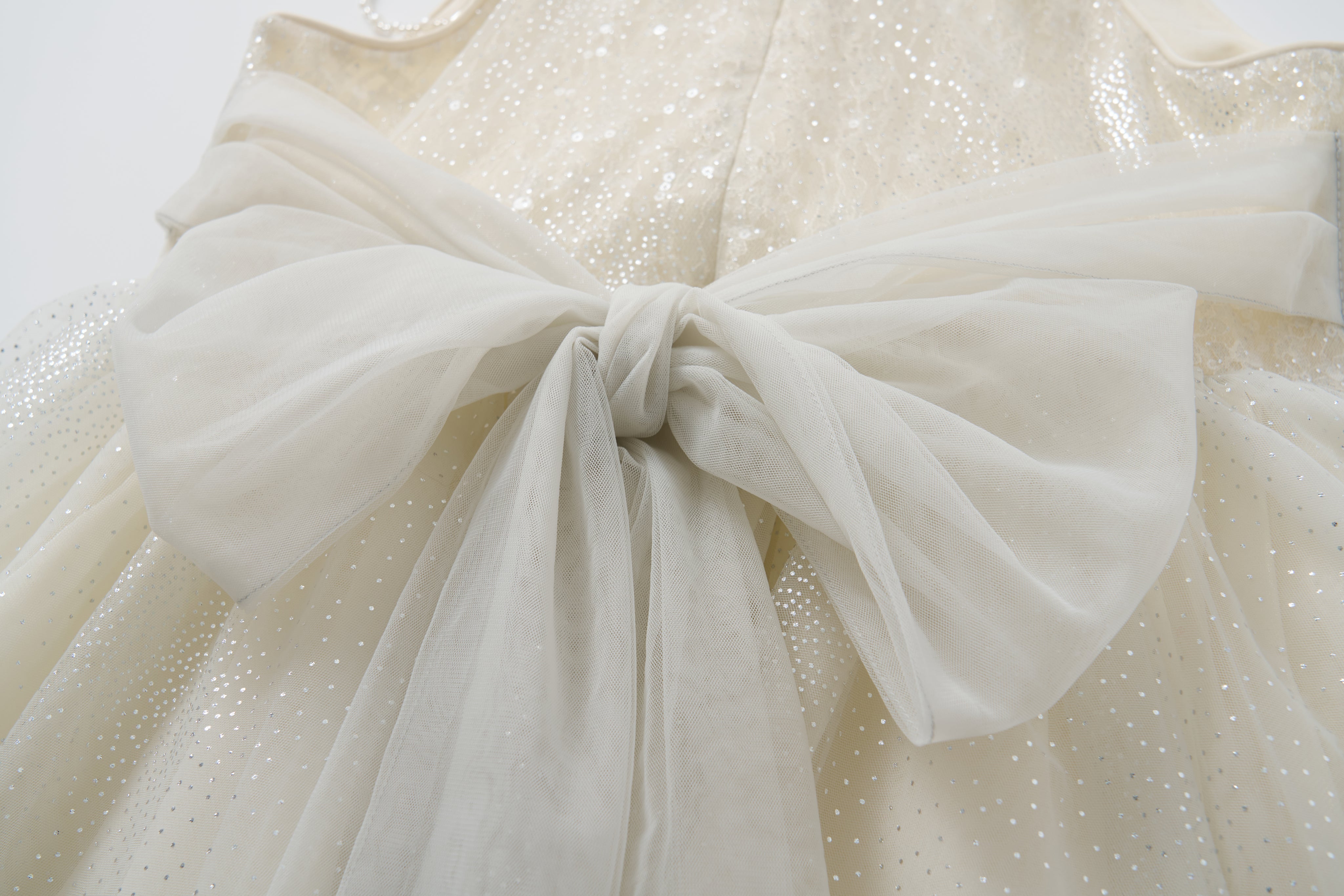 Close-up of the Gilded Whisper Dress by KIKI and JOJO—a white halter-neck sequin dress with a large, sheer bow elegantly tied at the back.