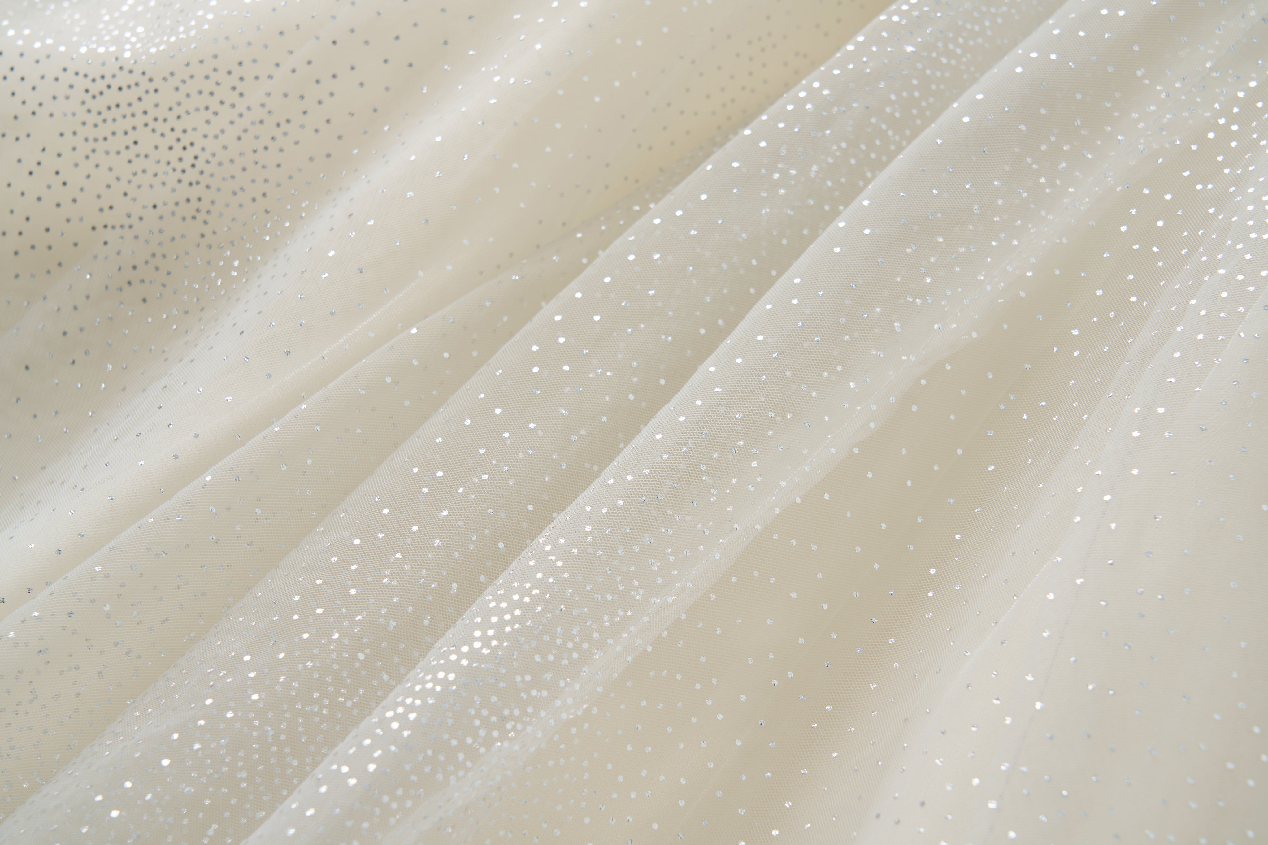 Close-up of sheer, off-white fabric adorned with small, silver dots, showcasing the delicate detailing on the Gilded Whisper Dress by KIKI and JOJO.