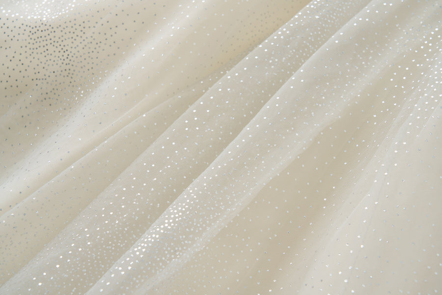Close-up of sheer, off-white fabric adorned with small, silver dots, showcasing the delicate detailing on the Gilded Whisper Dress by KIKI and JOJO.