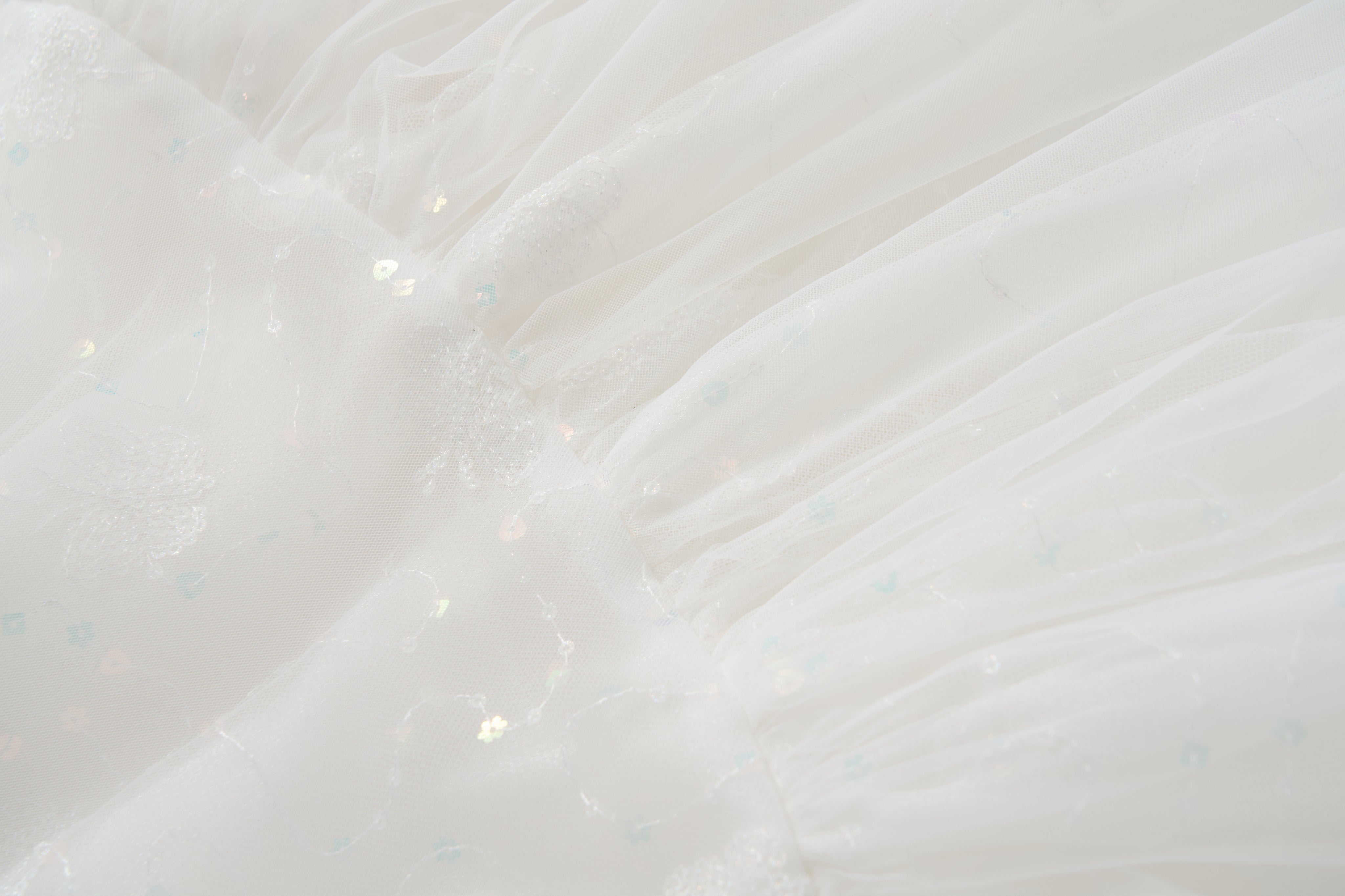 Close-up of white sheer fabric with subtle floral patterns and iridescent sequins, softly pleated—ideal for the KIKI and JOJO Butterfly Whispers Dress.