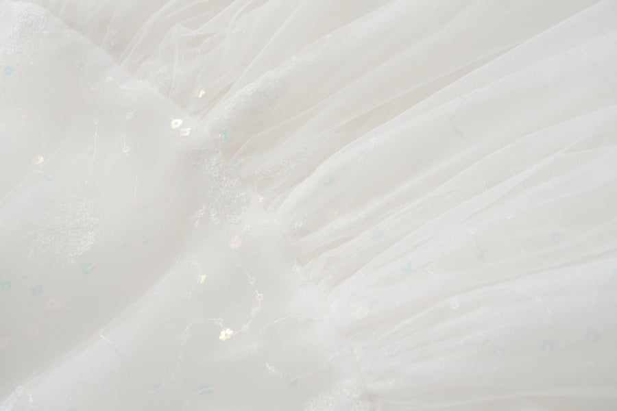 Close-up of white sheer fabric with subtle floral patterns and iridescent sequins, softly pleated—ideal for the KIKI and JOJO Butterfly Whispers Dress.