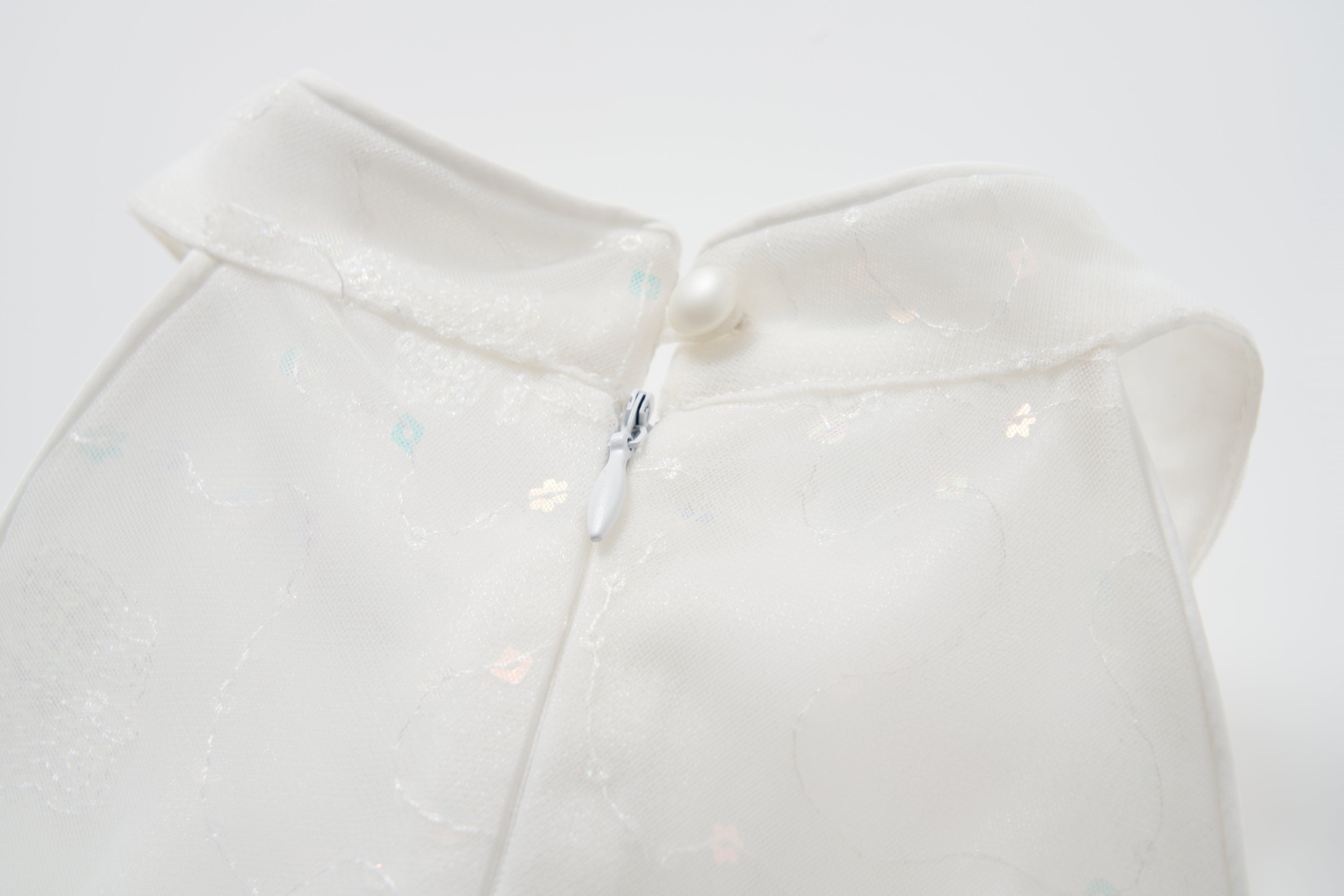 Close-up of the back of the KIKI and JOJO Butterfly Whispers Dress in white, featuring a halter style with a small zipper and button closure at the collar.